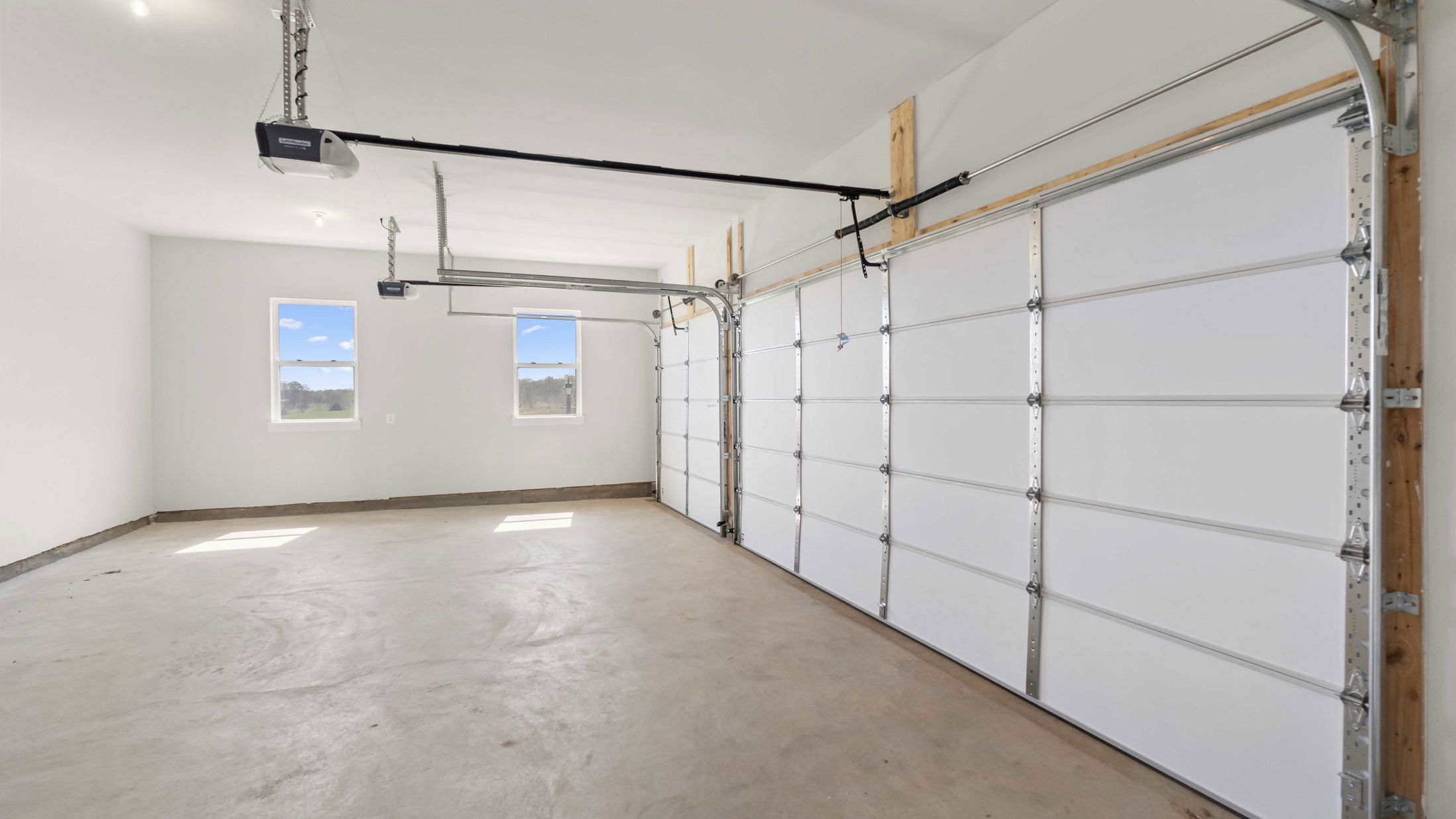 Empty two-car garage with white walls, large windows, and overhead doors.