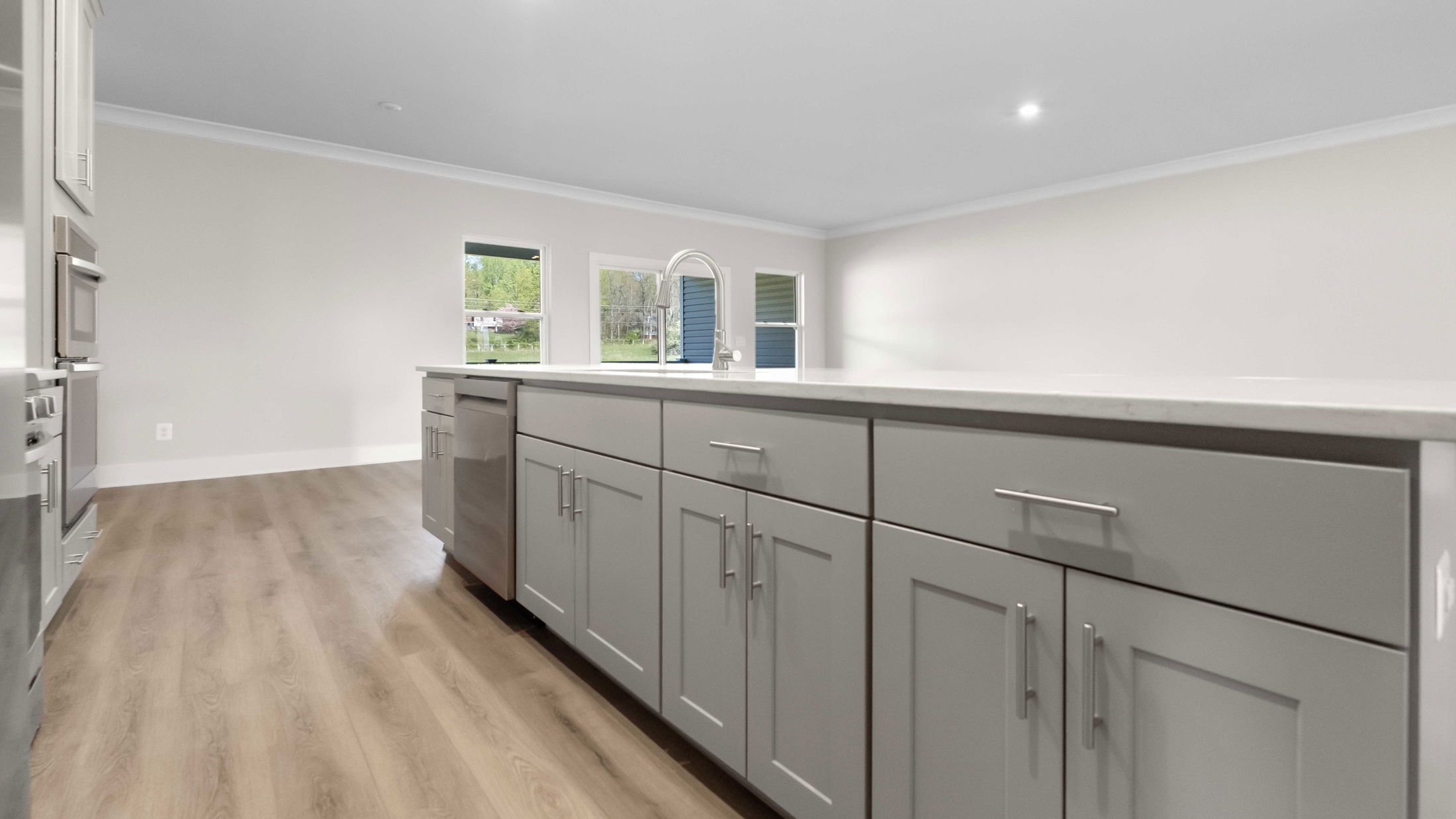 Modern kitchen with light gray cabinets, sleek countertops, and wood flooring, featuring stainless steel appliances and large windows.