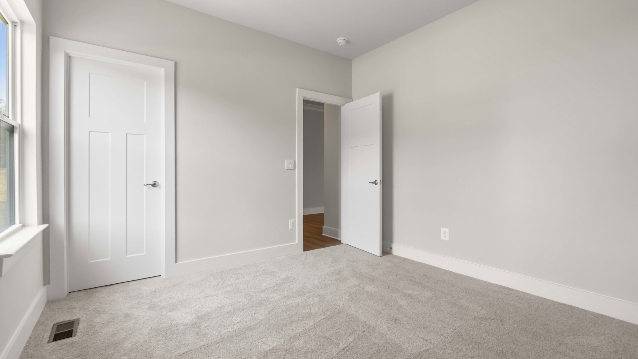 Empty room with light gray walls, a soft carpeted floor, and a white door slightly ajar.