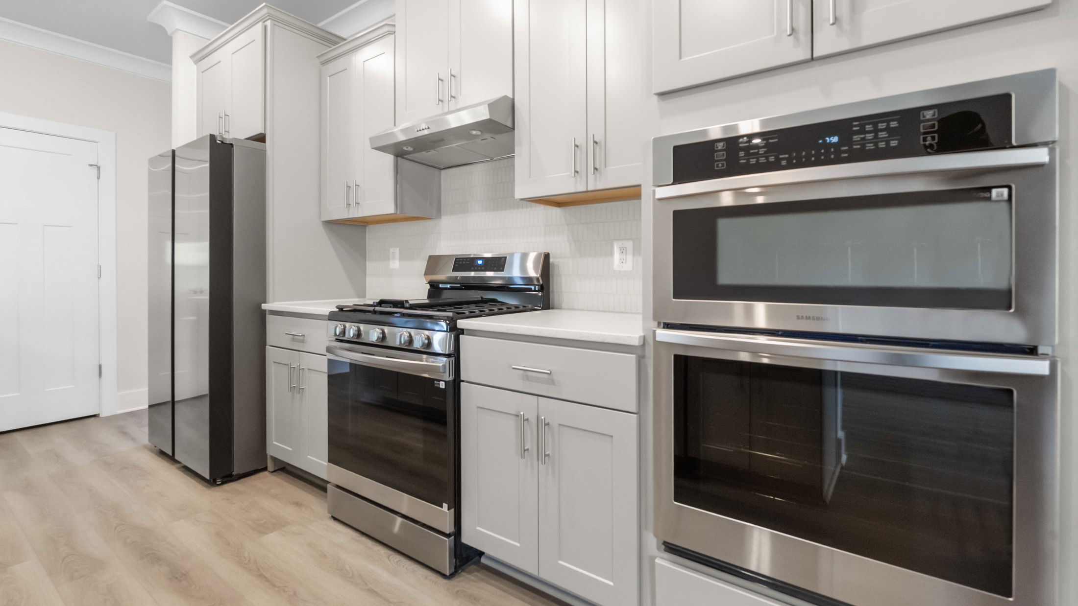 Modern kitchen with stainless steel appliances, white cabinets, and light wood flooring.