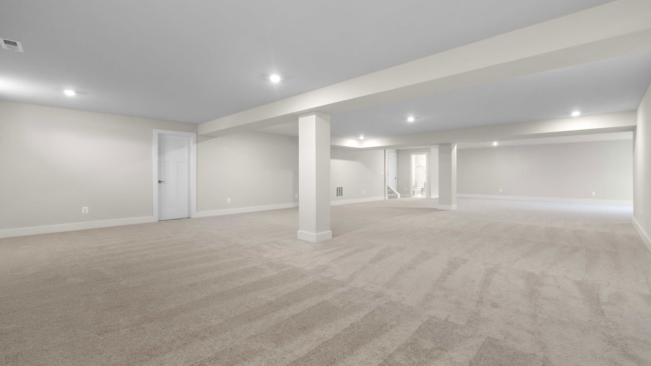 Spacious, modern finished basement with beige carpeting and recessed lighting.