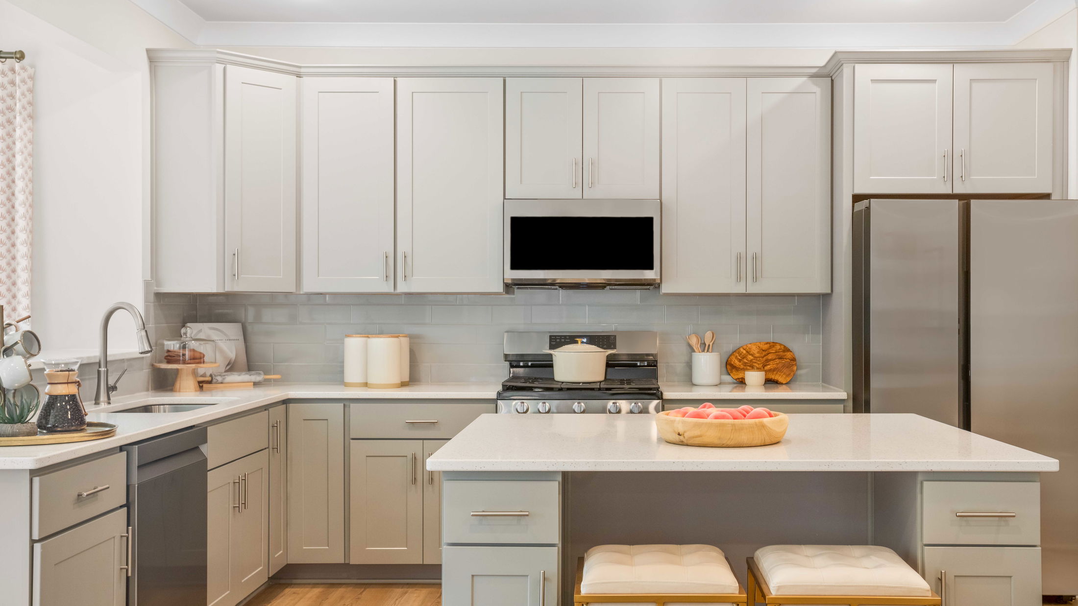 Modern kitchen with light gray cabinets, stainless steel appliances, and a white countertop island with stools.