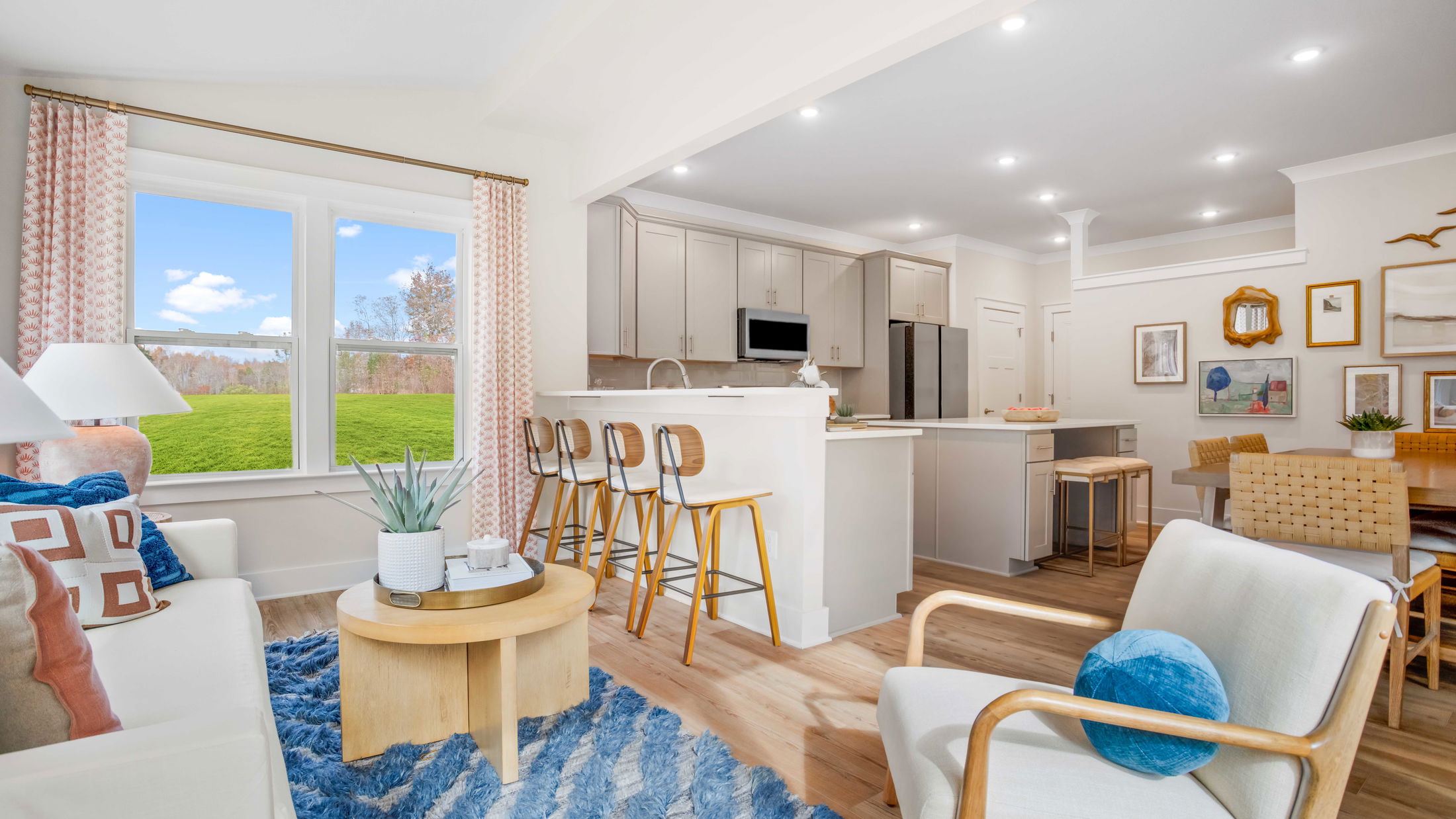 Bright and modern open-concept living room and kitchen with stylish decor, featuring wooden furniture, patterned curtains, and a blue accent rug.
