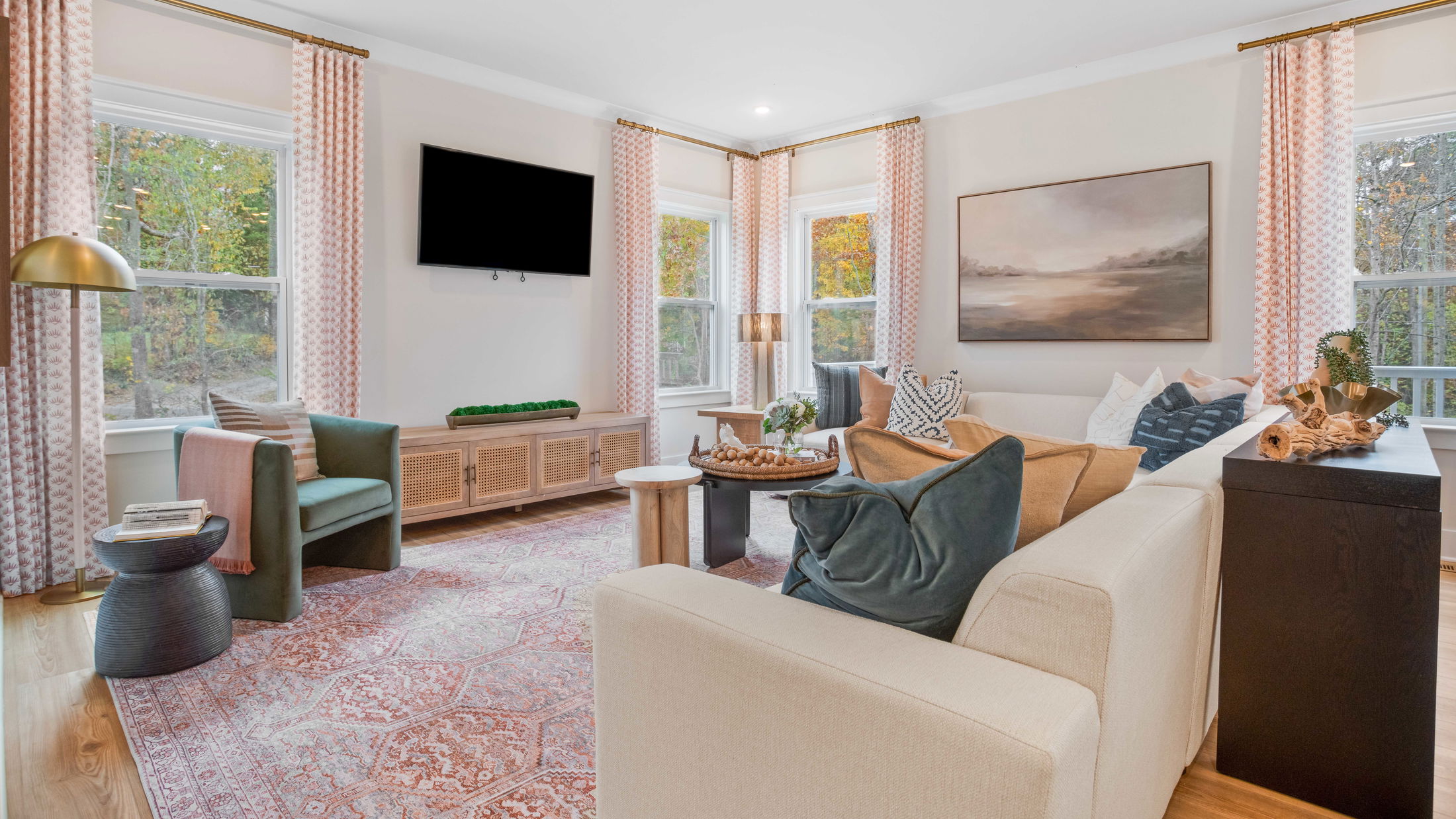 Modern living room with a cozy sectional sofa, accented by patterned pillows and a decorative rug, featuring large windows and contemporary decor.