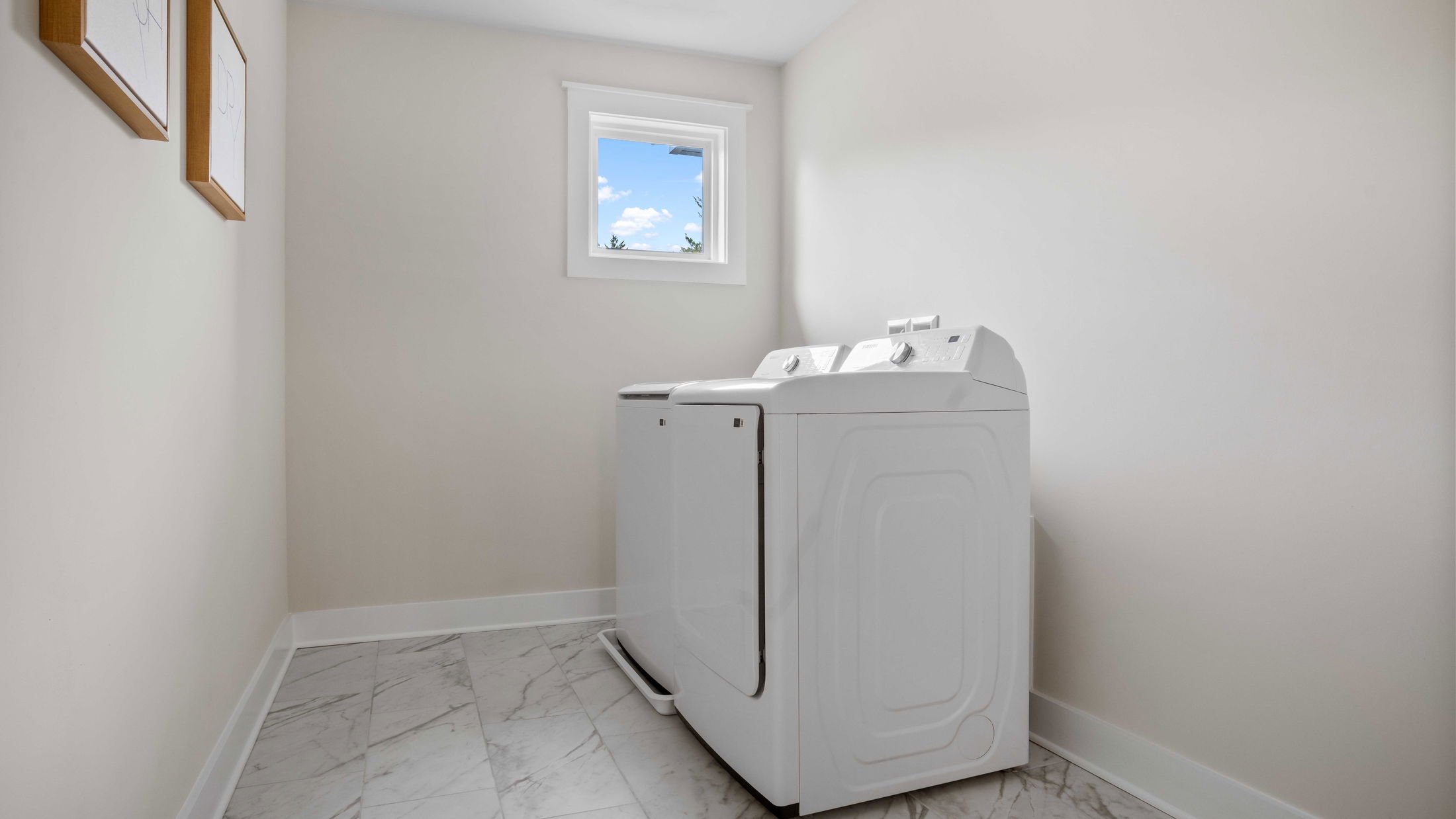 Modern laundry room with white washer and dryer against a light-colored wall and marble tile flooring.