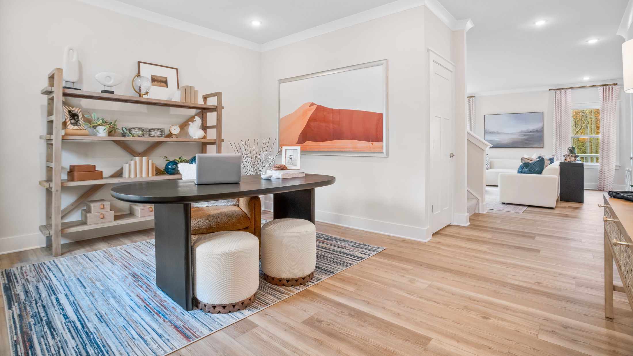 Modern home office and living room area with stylish decor, wooden shelving, dark table, and a colorful rug.