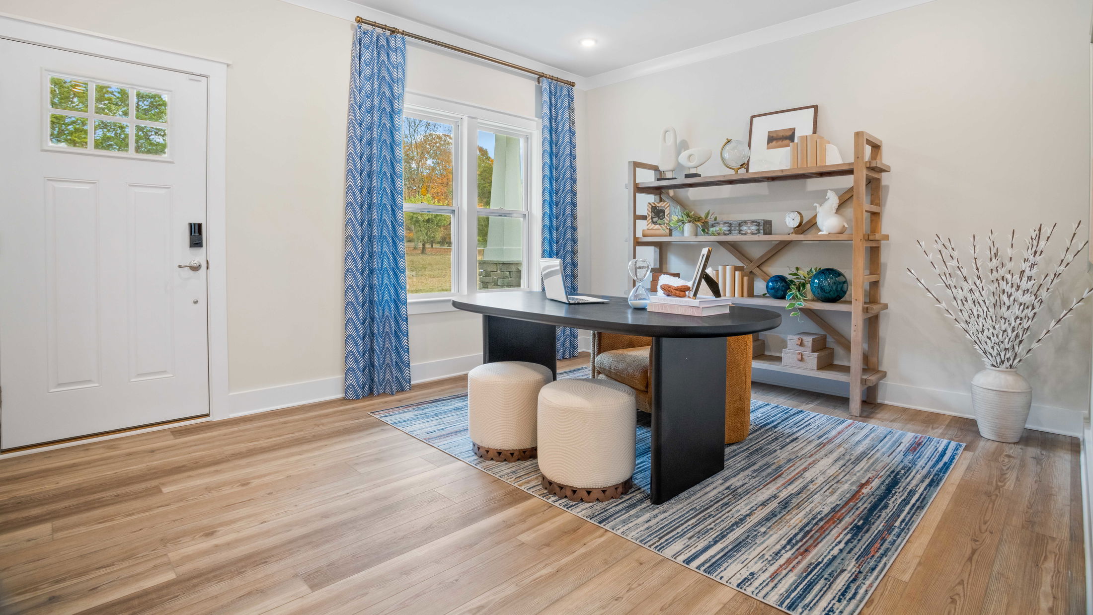 Modern home office with wooden shelves, blue curtains, a black desk, and contemporary decor.