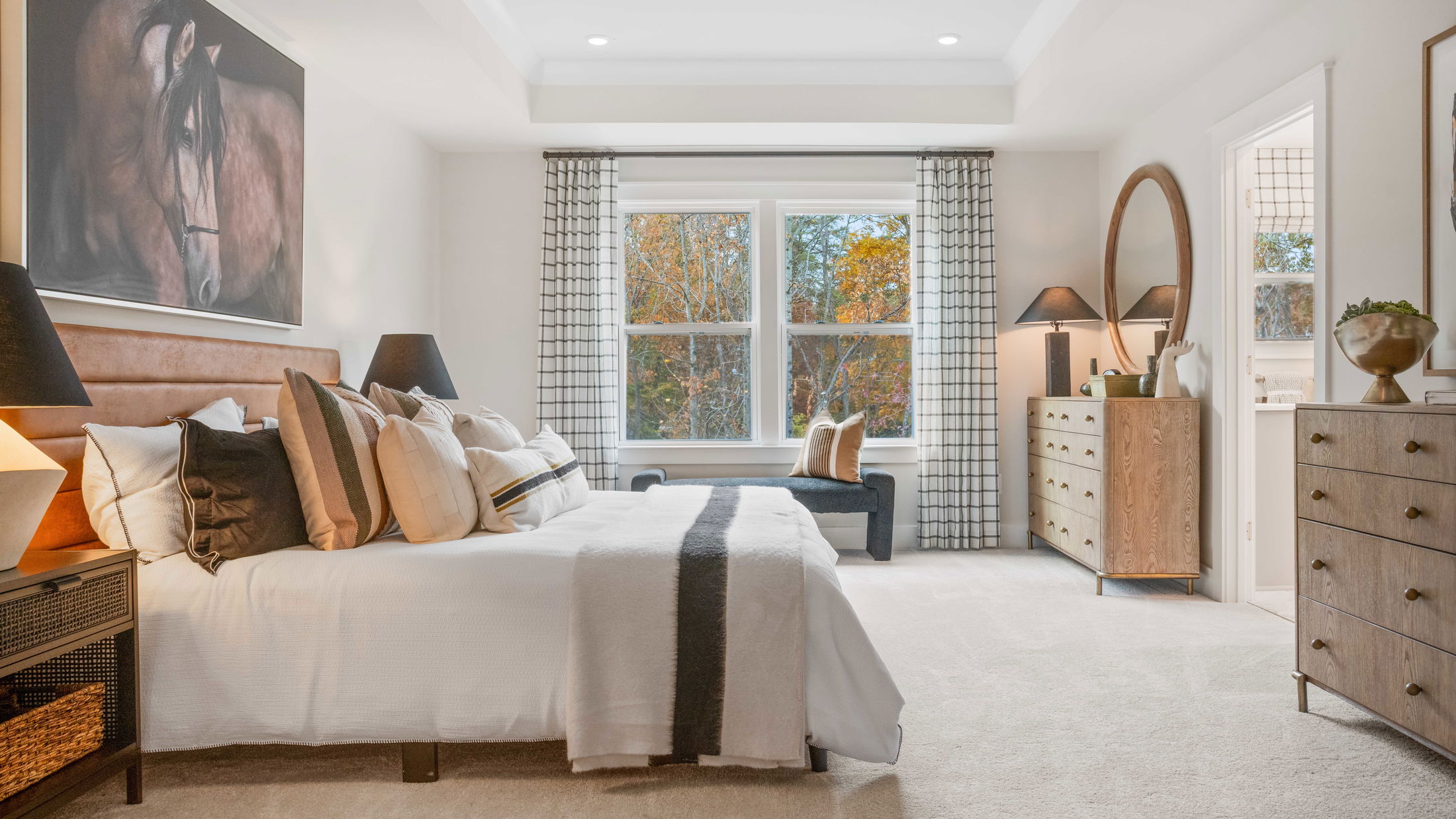 Modern bedroom with a stylish brown bed, cozy pillows, accent horse artwork, and natural light from large windows.