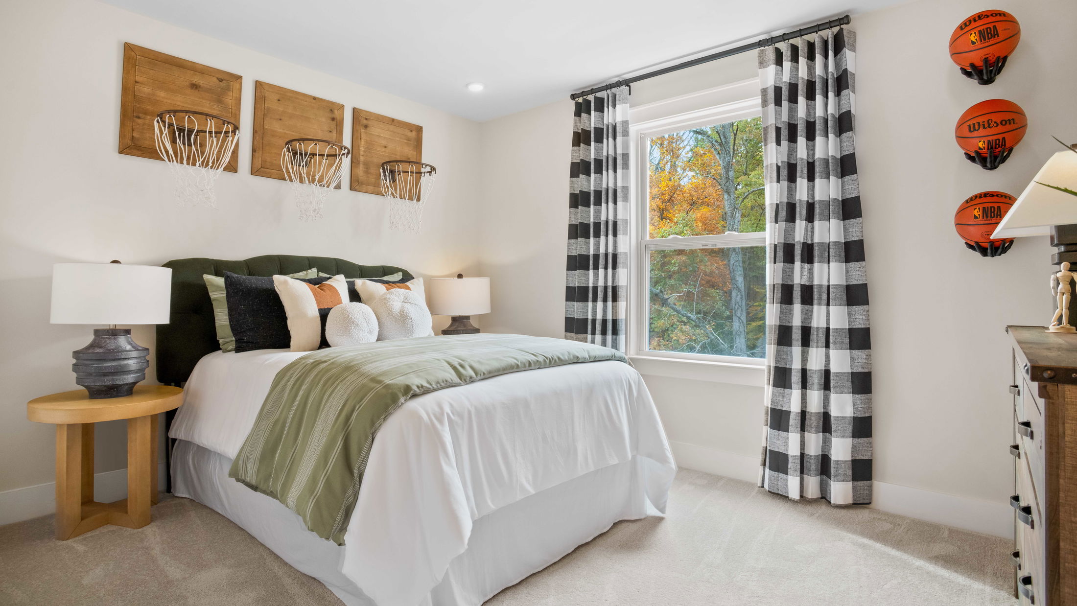 Cozy bedroom with basketball-themed decor, featuring mounted basketballs and hoop wall art, complemented by earthy-toned bedding and a large window with checkered curtains.
