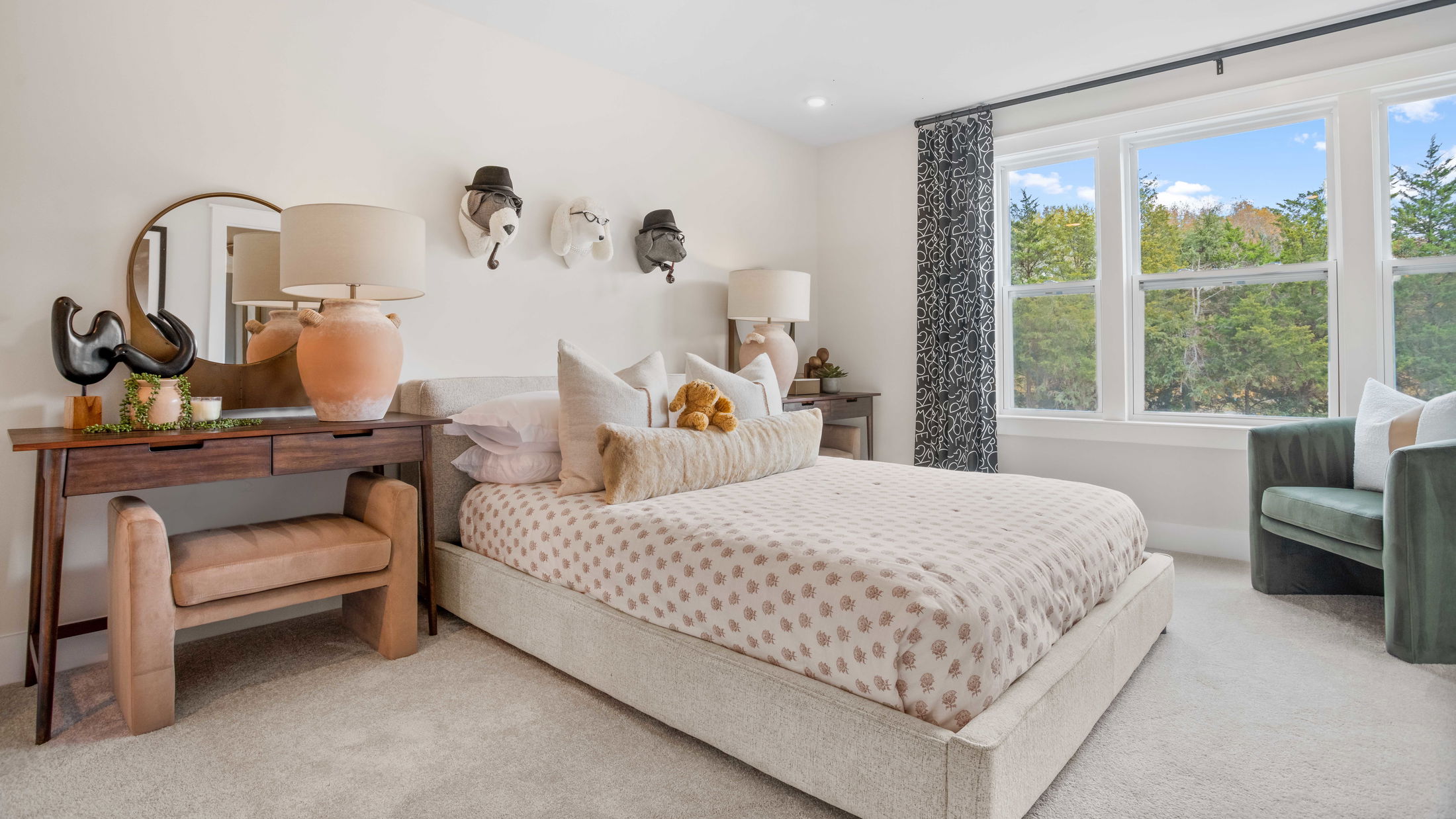 Modern bedroom with a patterned bed, decorative wall art, wooden furniture, and large windows overlooking trees.