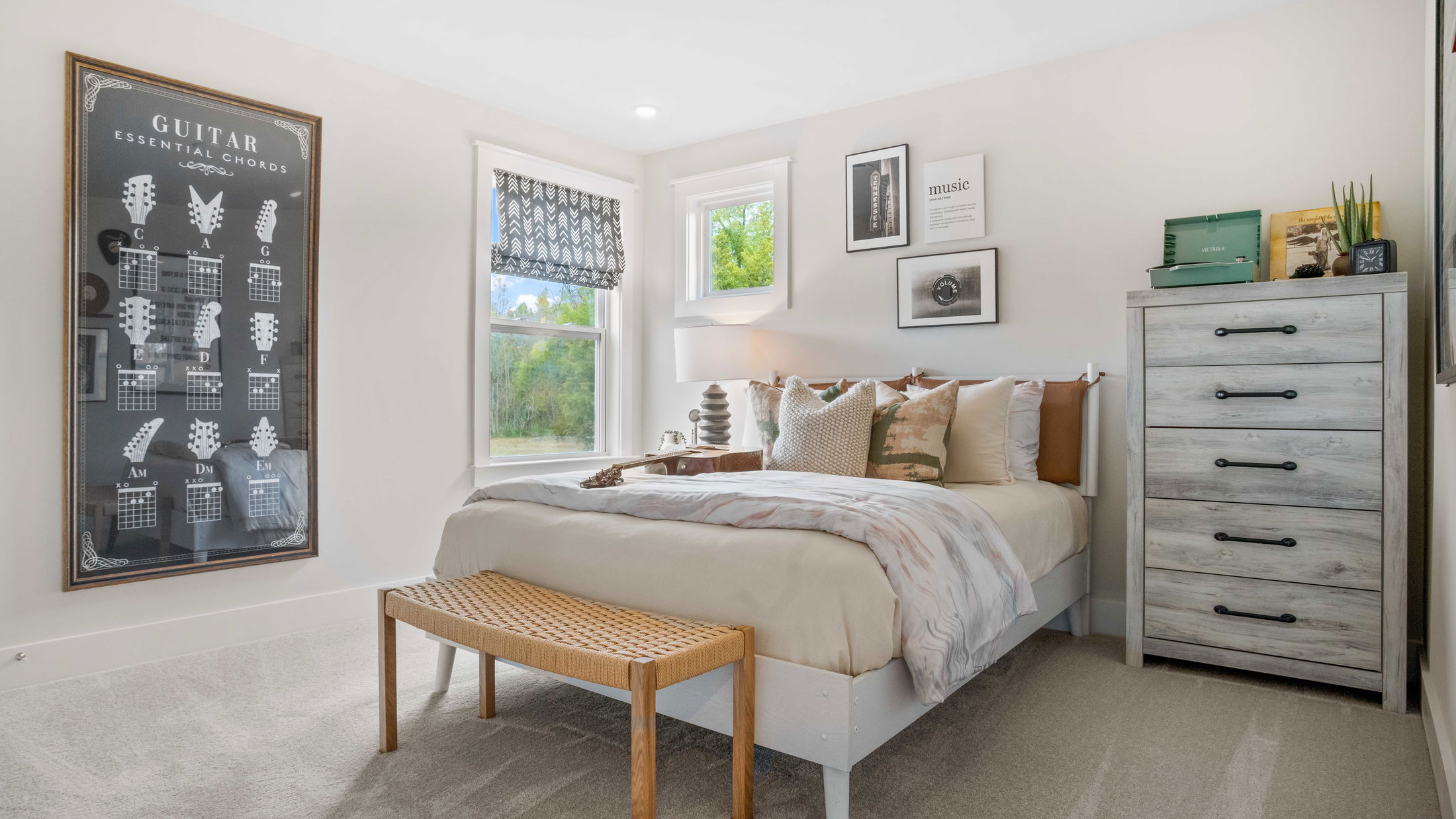 Modern bedroom with beige and white decor, featuring a guitar-themed wall art, cushioned bed, woven bench, and a rustic dresser.