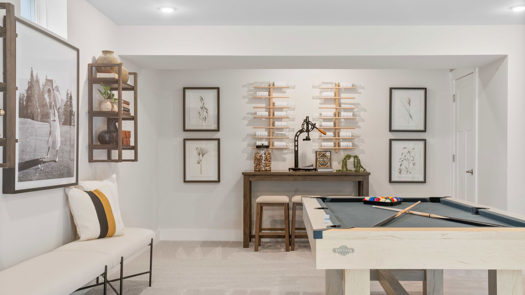 Stylish basement entertainment room with a pool table, wall art, and shelving for decor and wine storage.