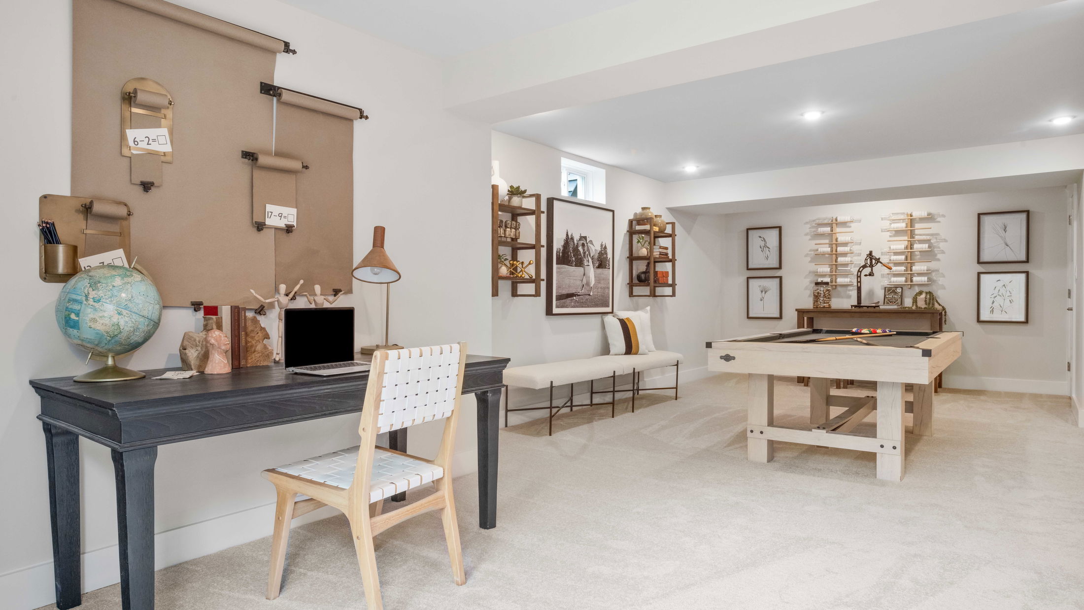 Modern basement home office and game room with a dark desk, globe, billiards table, and elegant wall decor.