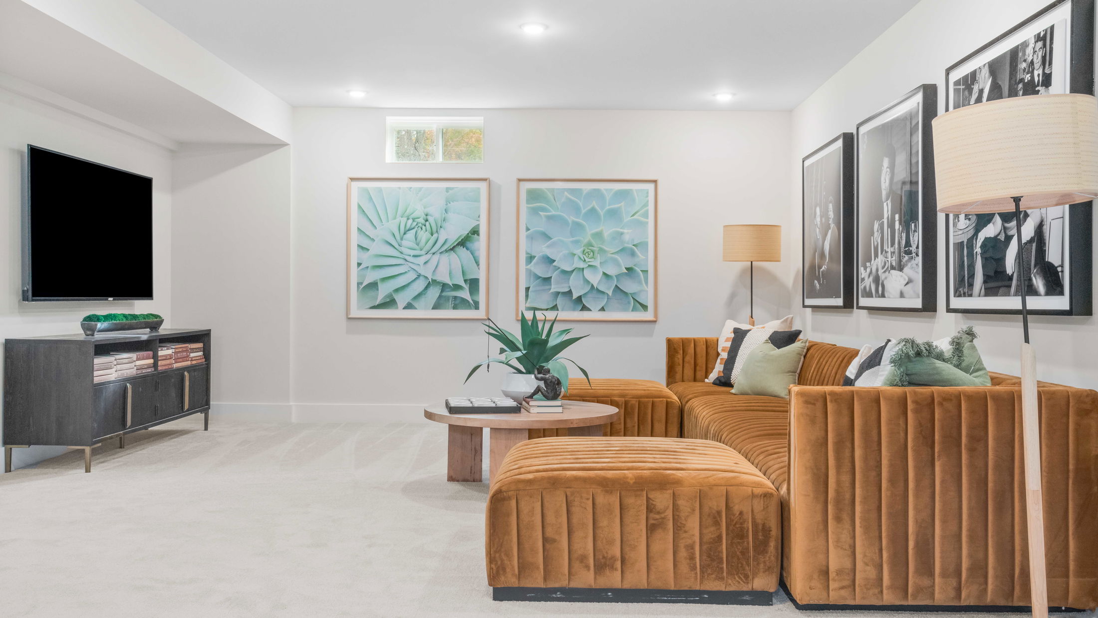 Stylish modern living room featuring a plush orange sectional sofa, framed botanical art, and large monochrome photographs, creating a cozy and elegant atmosphere.