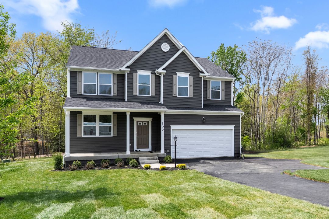 Modern two-story dark gray house with a manicured lawn and attached white garage in a suburban neighborhood.
