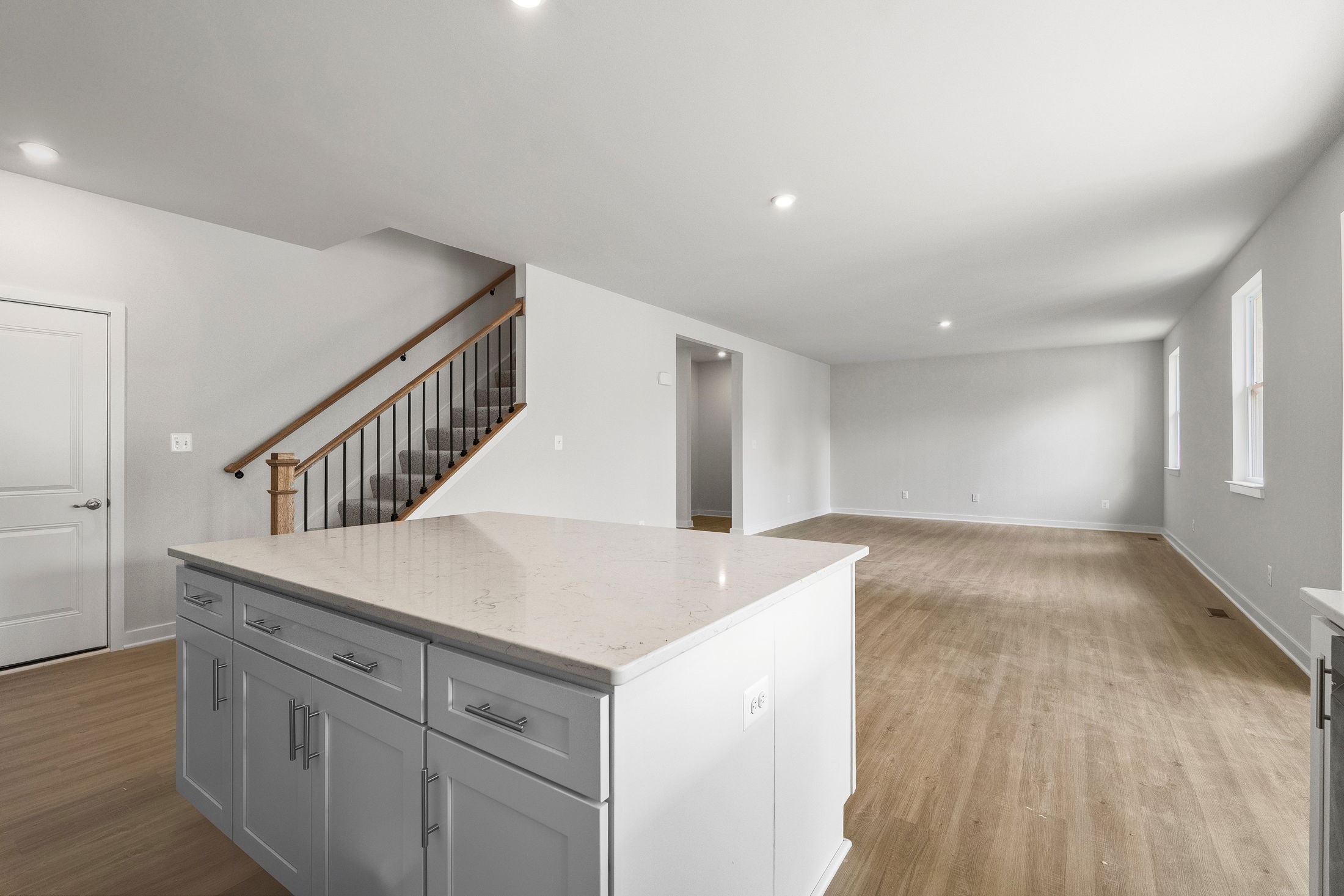 Spacious modern interior of an unfurnished home with hardwood floors, a white kitchen island, and a staircase.