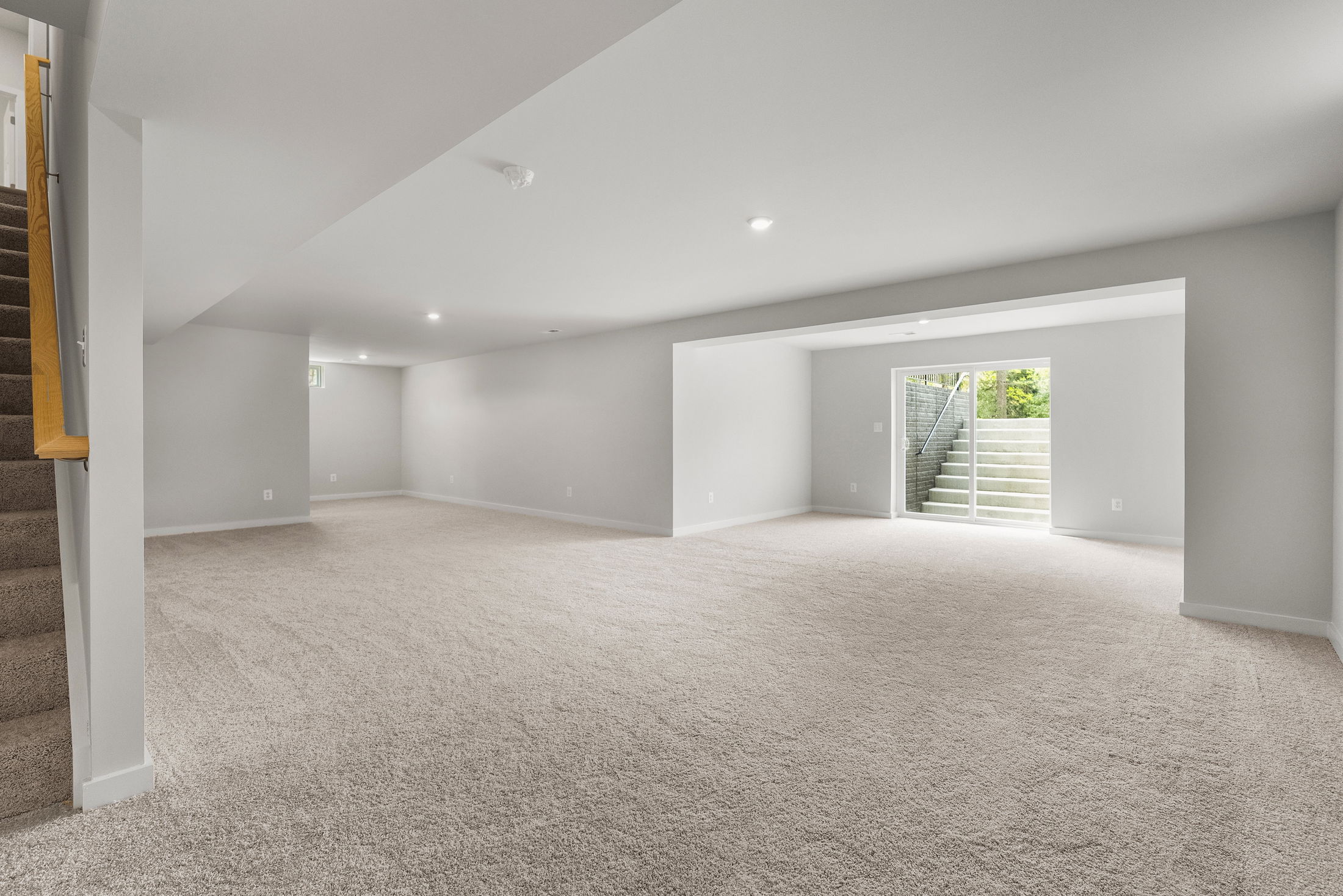 Spacious and modern finished basement with carpet flooring, recessed lighting, and a walkout door leading to an outdoor staircase.