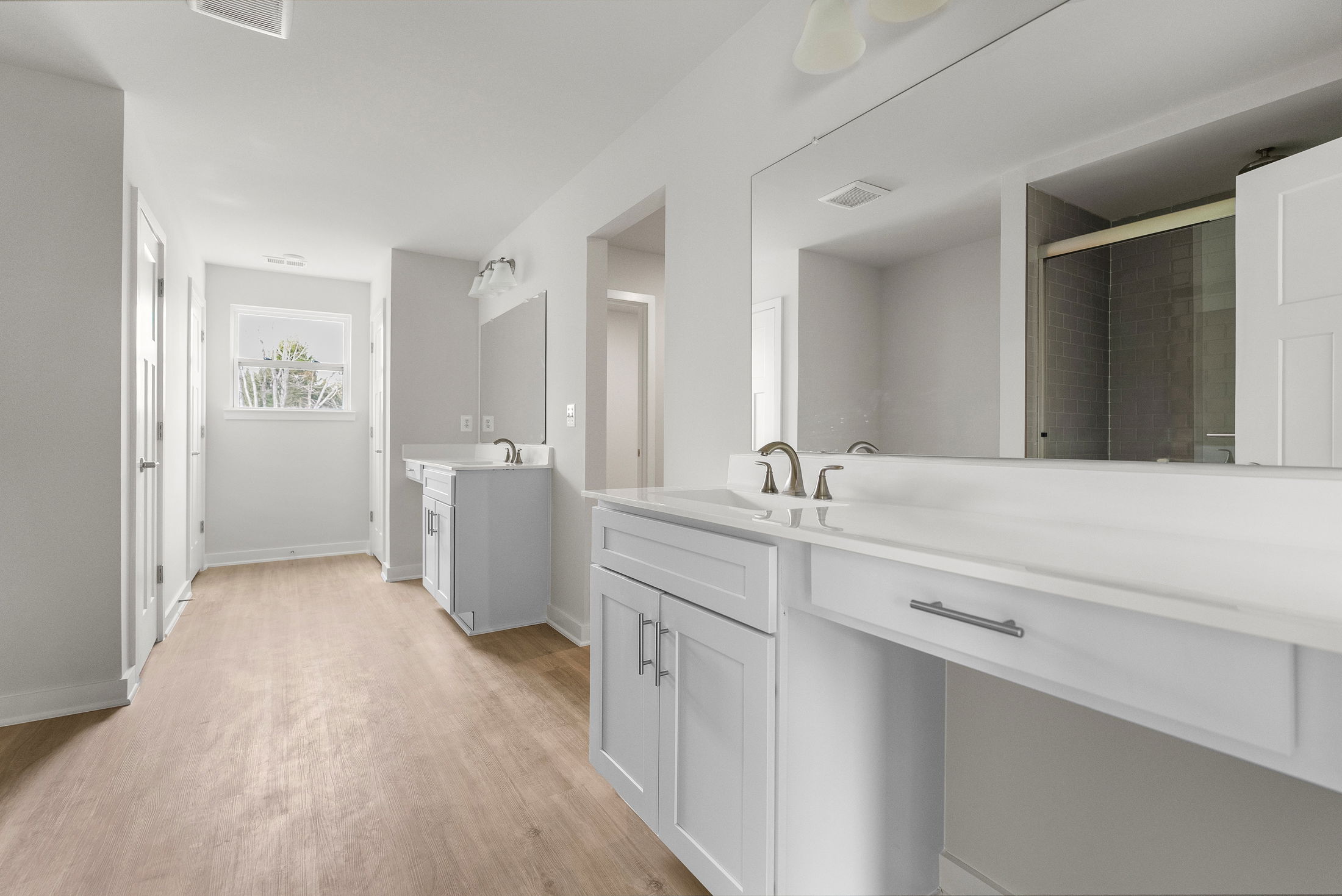 Modern bathroom interior with light gray cabinets, large mirrors, and wood-style flooring.