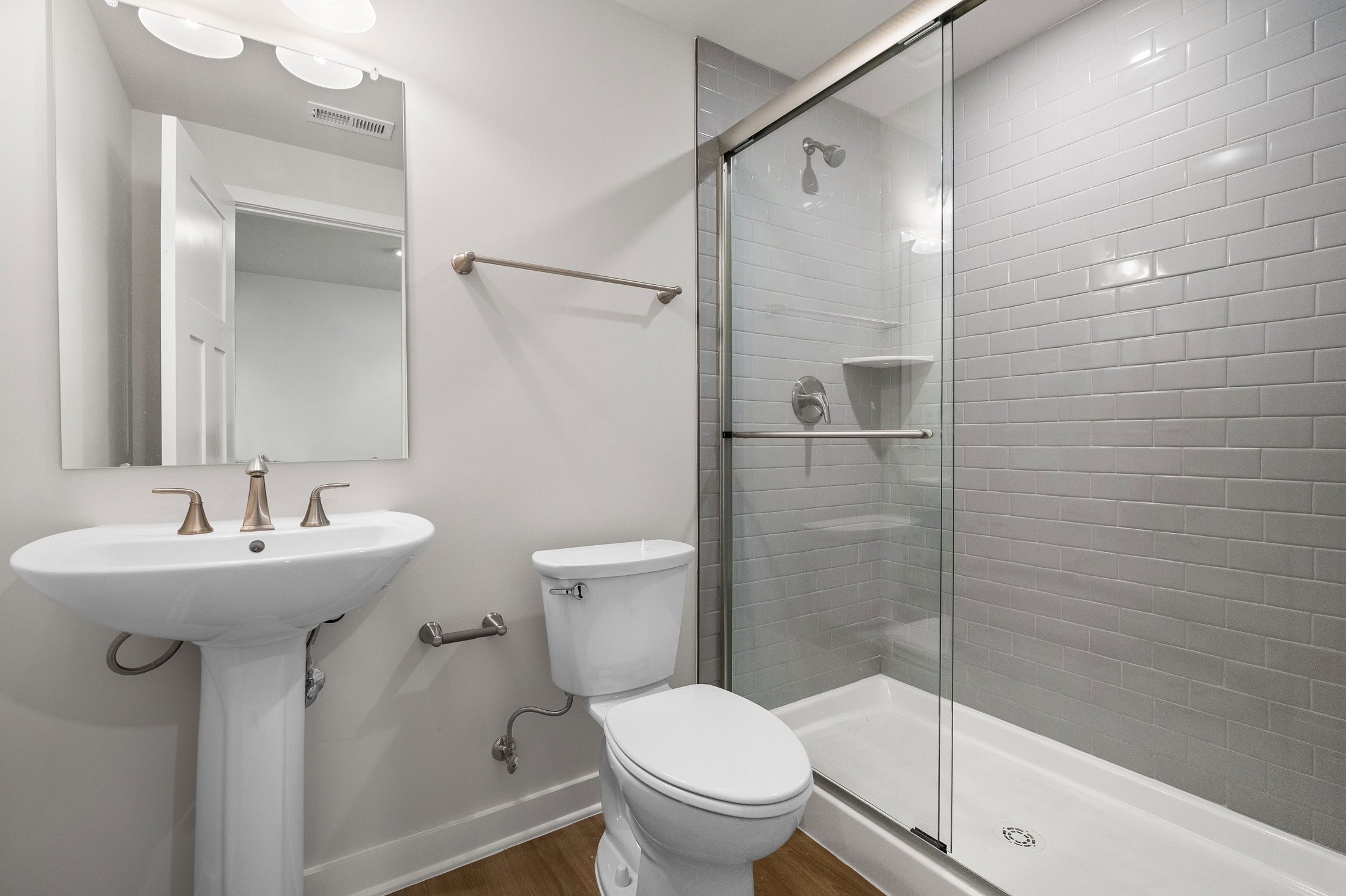 Modern bathroom with a pedestal sink, toilet, and a glass-enclosed shower featuring subway tile walls.