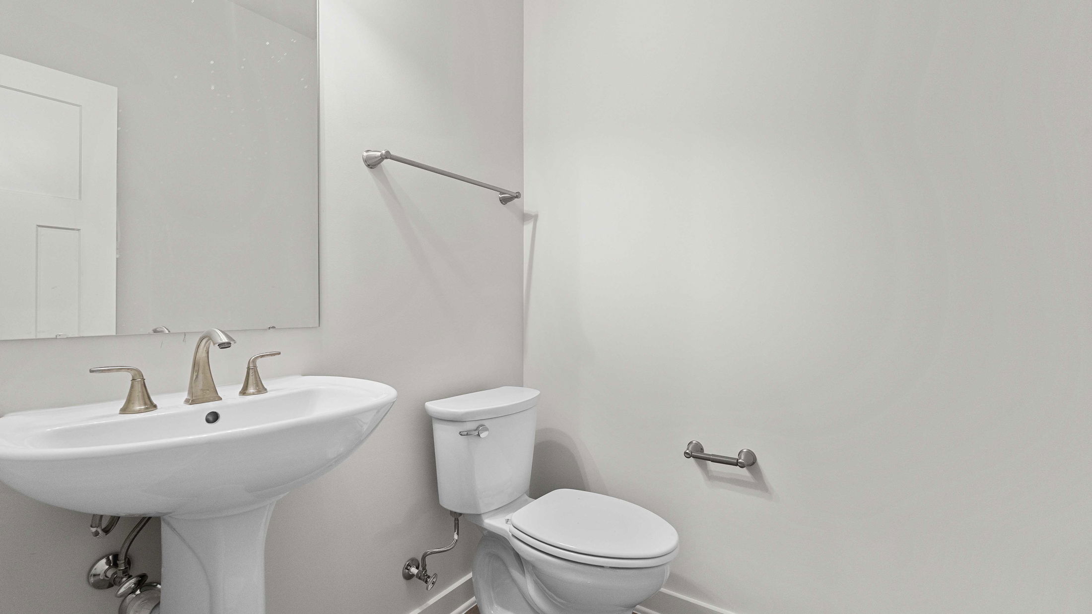 Modern bathroom with white pedestal sink and toilet against light gray walls.