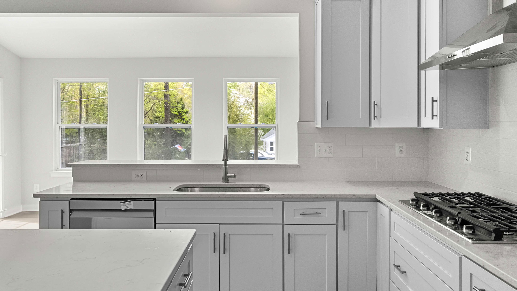 Modern kitchen interior featuring sleek white cabinets, stainless steel appliances, and large windows with a view of greenery.