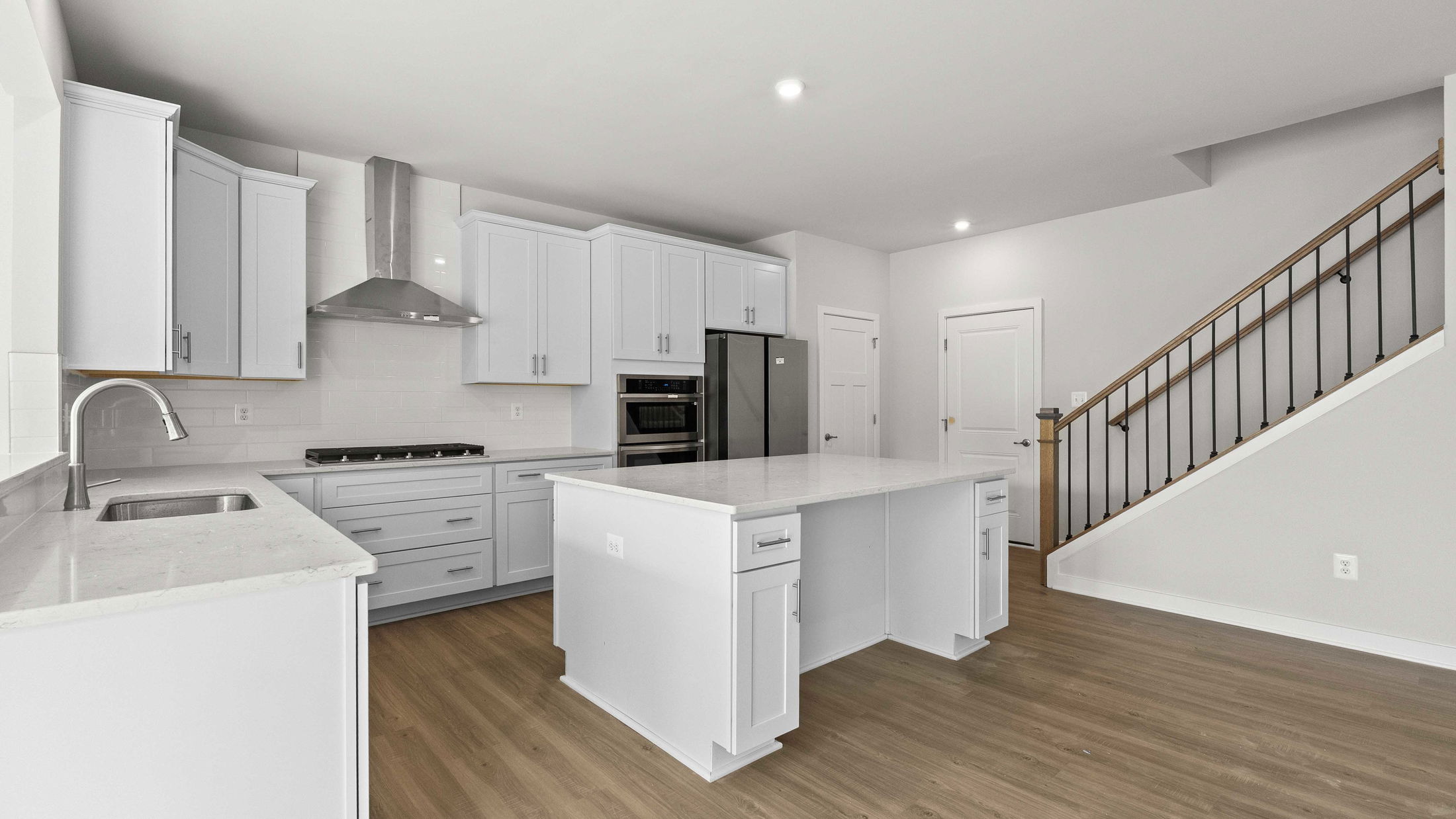 Modern kitchen interior with white cabinetry, stainless steel appliances, and a central island featuring a marble countertop.