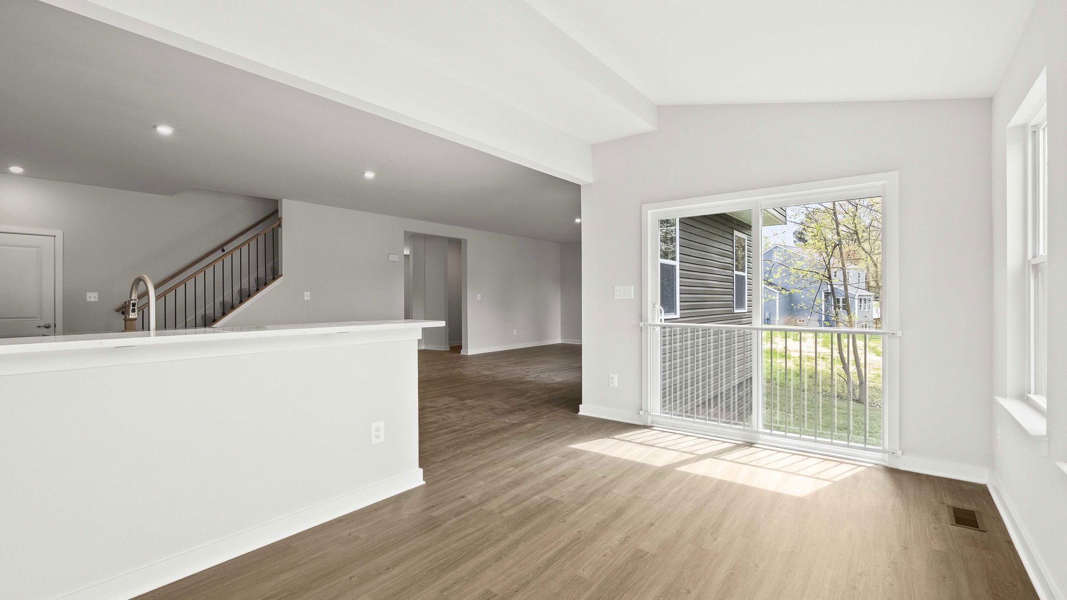 Open concept living area with hardwood floors, white walls, a staircase, and large sliding glass doors leading to a balcony with a view of the backyard.