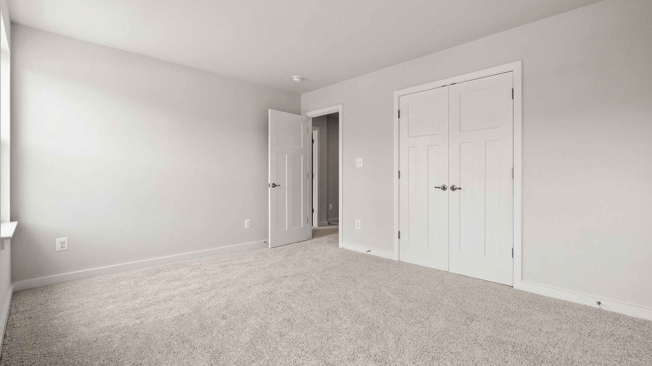 Empty room with light gray walls, beige carpet, and white double doors for closets.