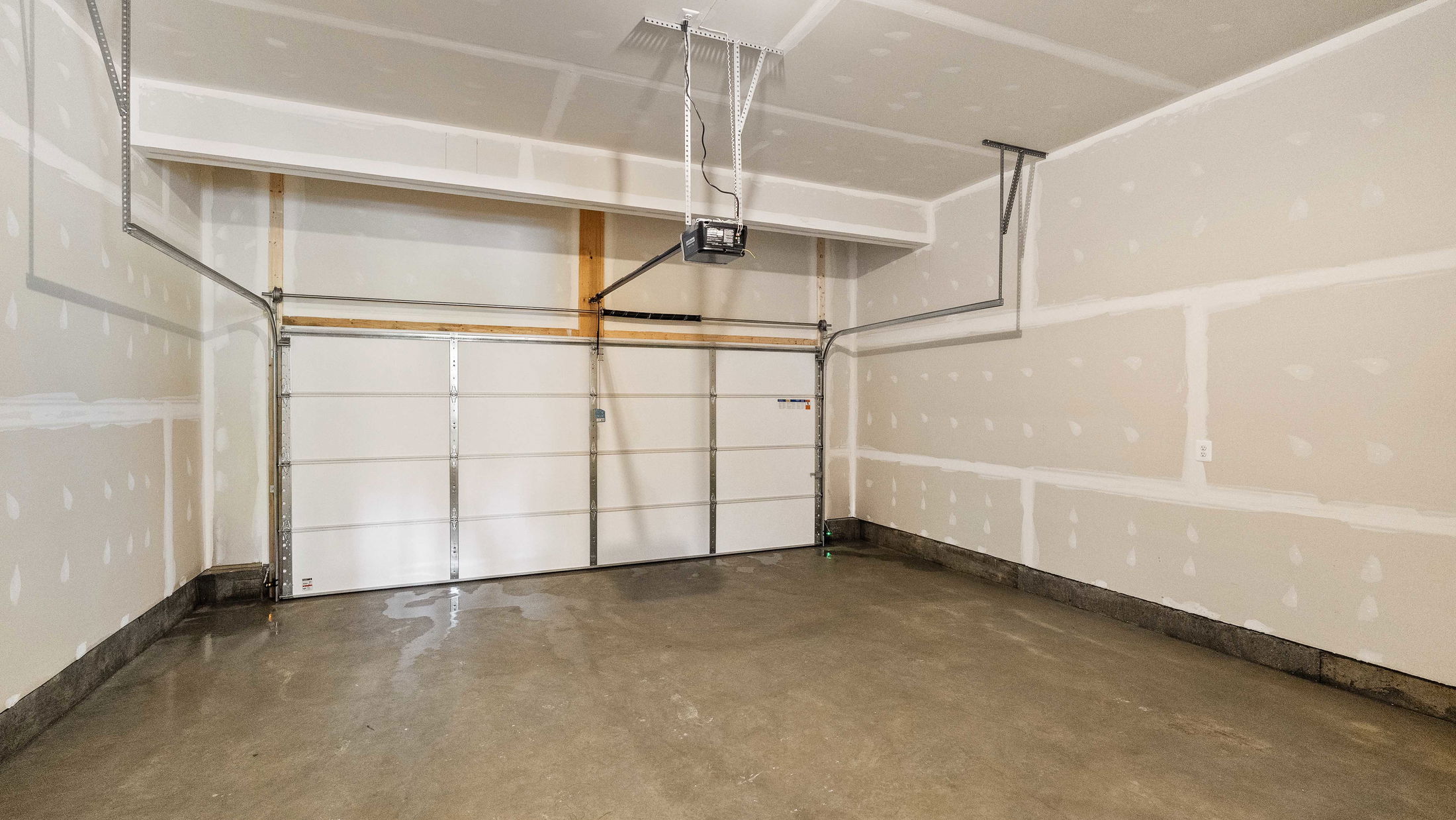 Empty residential garage interior with unfinished drywall and a closed garage door.