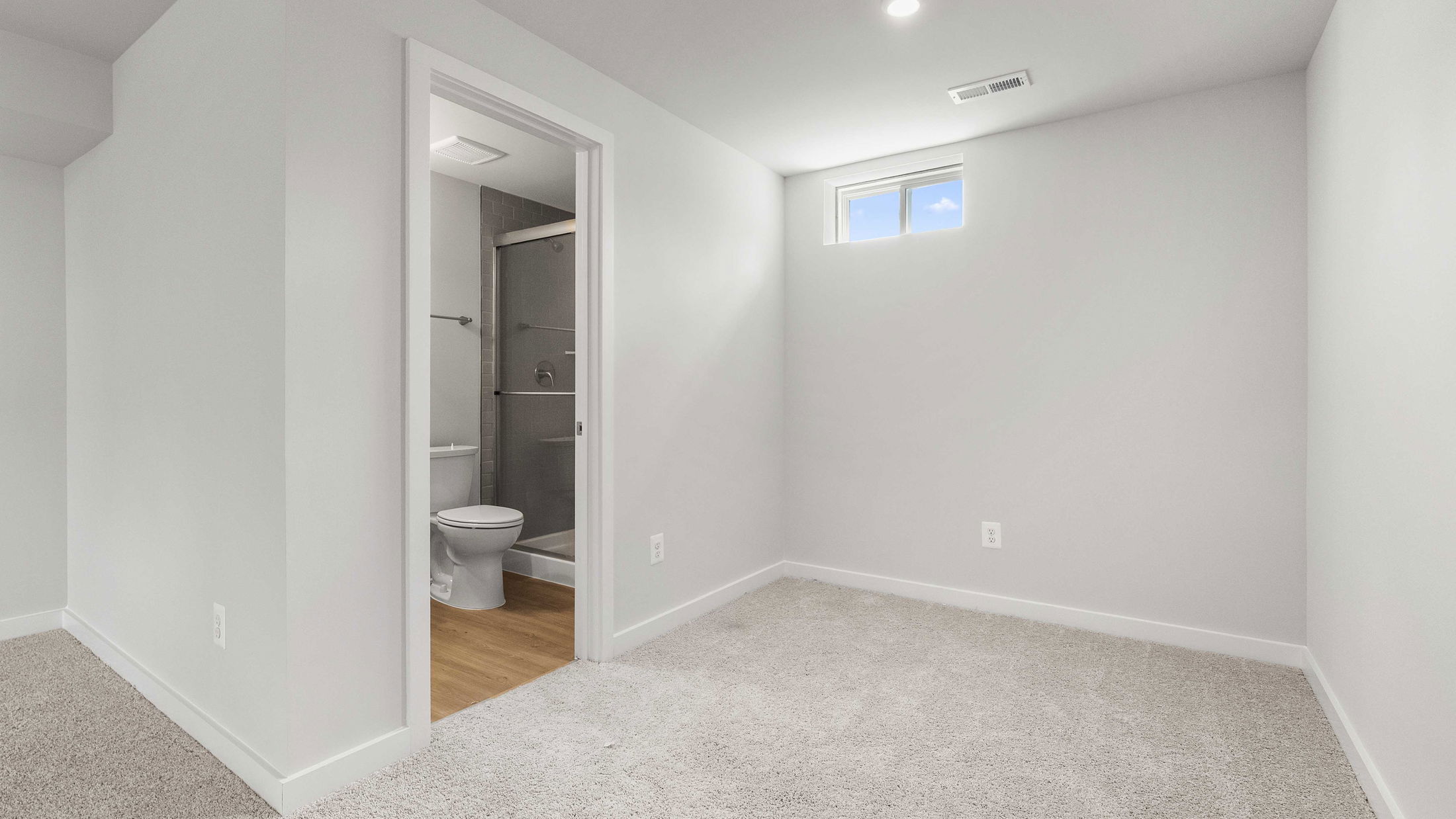 Modern, small carpeted room with an adjacent bathroom featuring a shower and toilet.