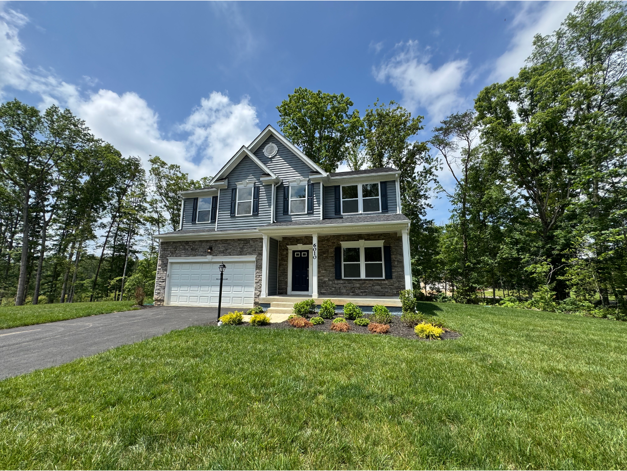 A two-story suburban house with a stone facade and garage, surrounded by lush greenery under a blue sky.