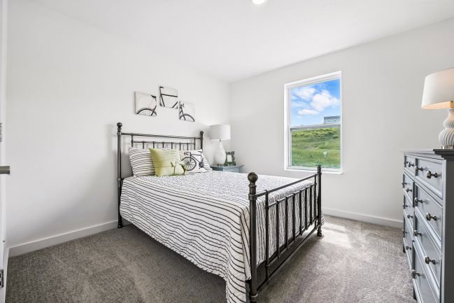 A modern bedroom featuring a metal bed frame, striped bedding, a bedside lamp, a dresser, and a window with a view of green fields.