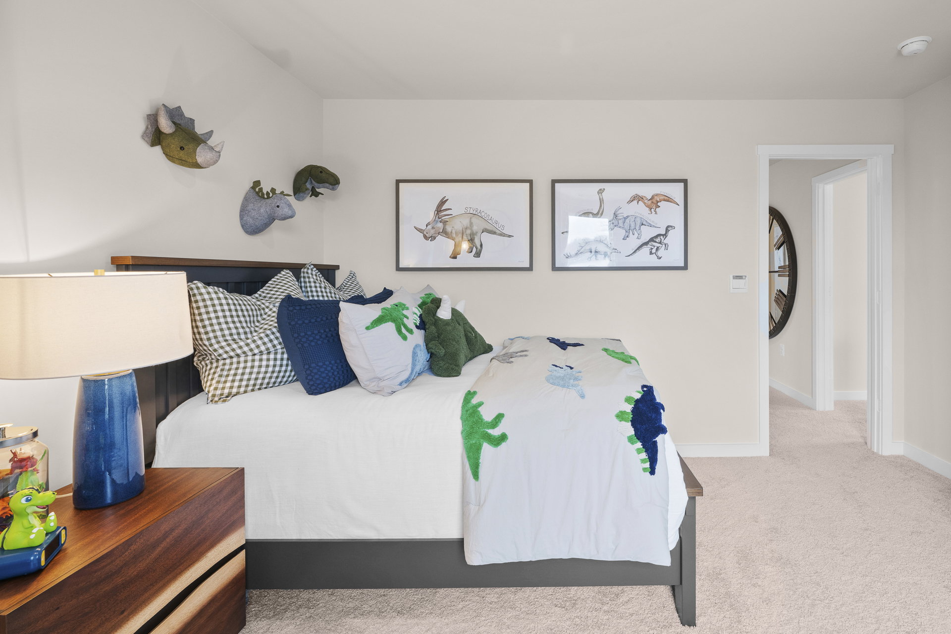 A cozy children's bedroom featuring a bed with colorful dinosaur-themed bedding, decorative pillows, and framed dinosaur artwork on the walls.