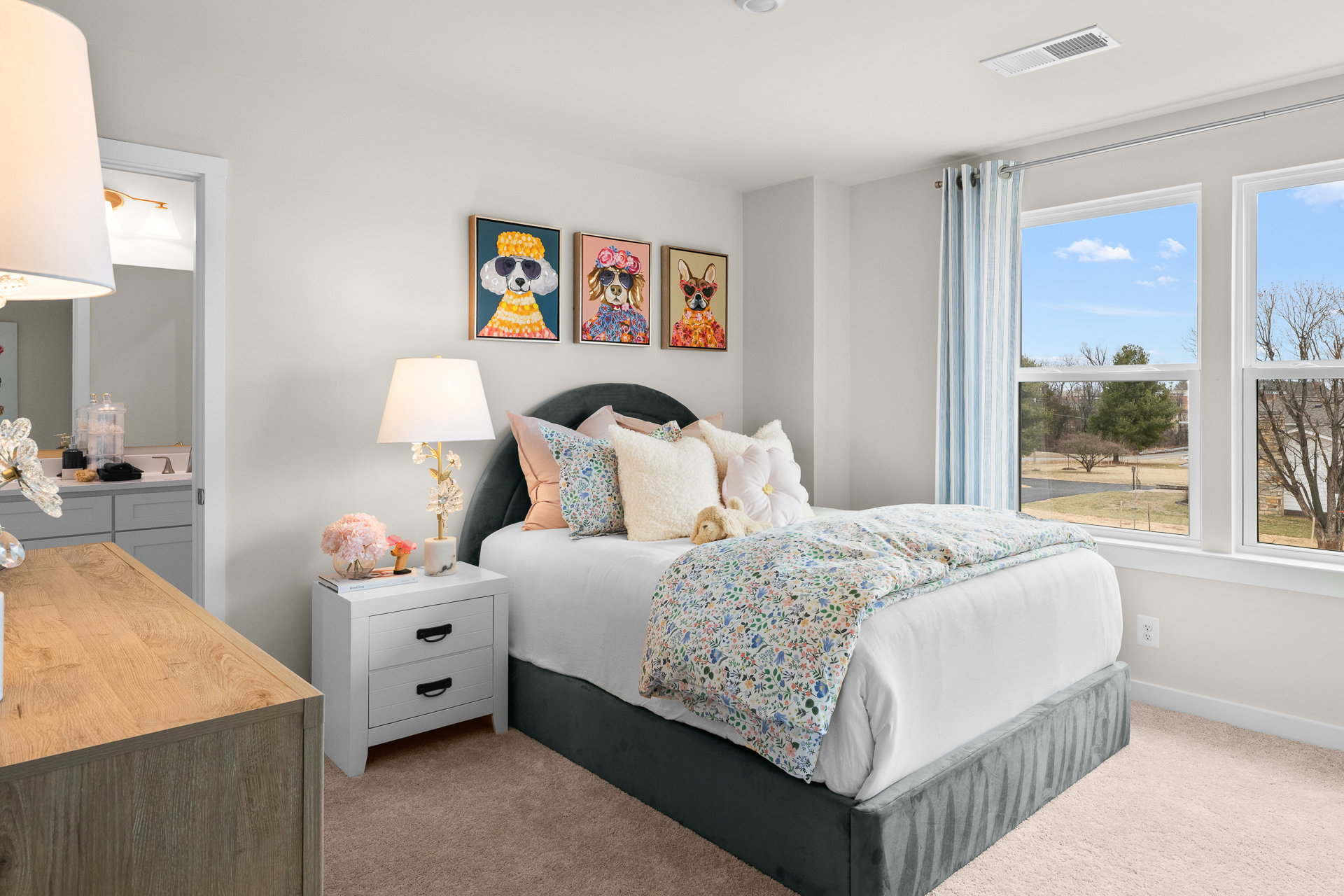 A cozy bedroom featuring a bed with decorative pillows, a bedside table with a lamp, and artwork on the walls.