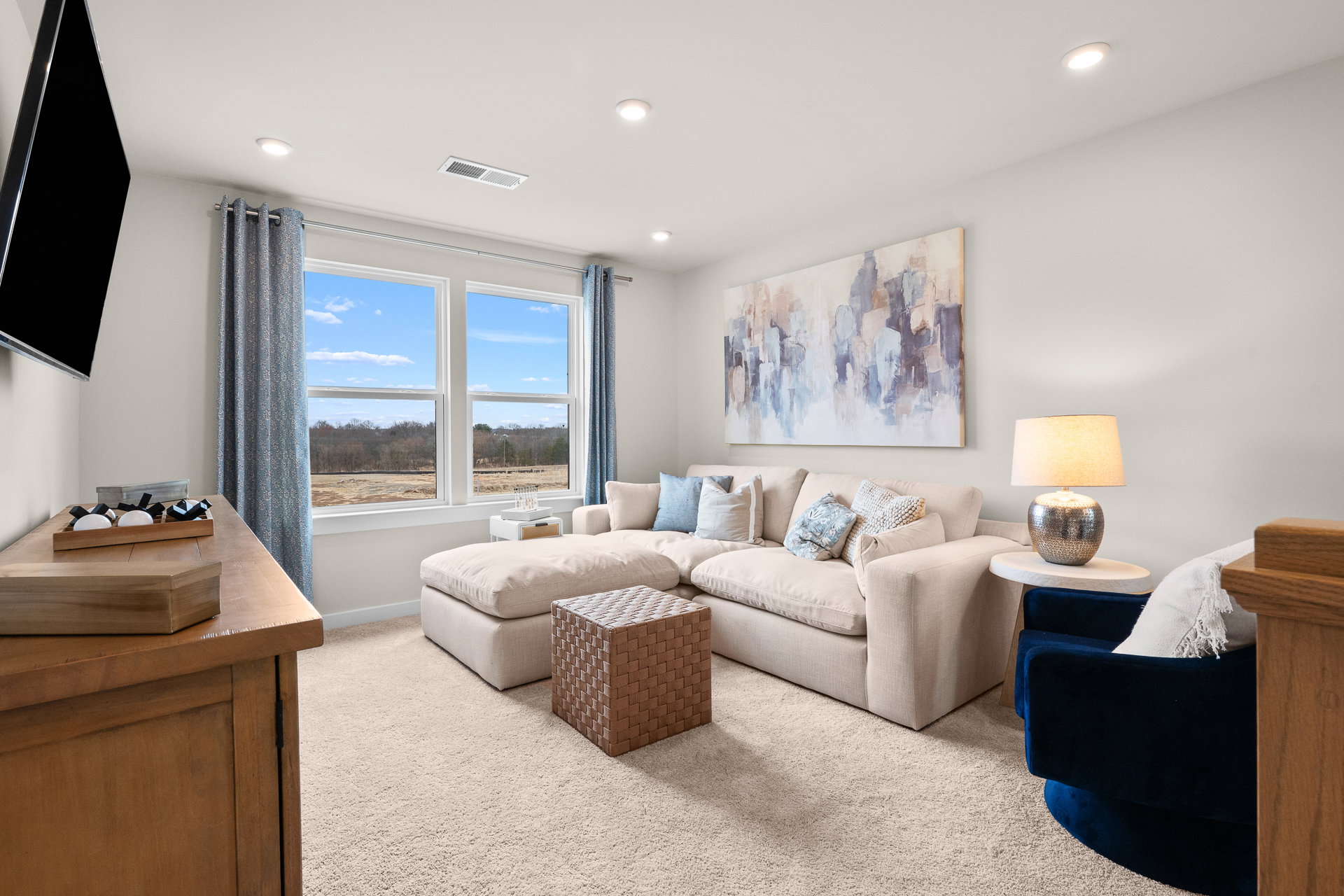 Cozy living room with a sectional sofa, decorative pillows, a blue armchair, a lamp, and a large window letting in natural light.