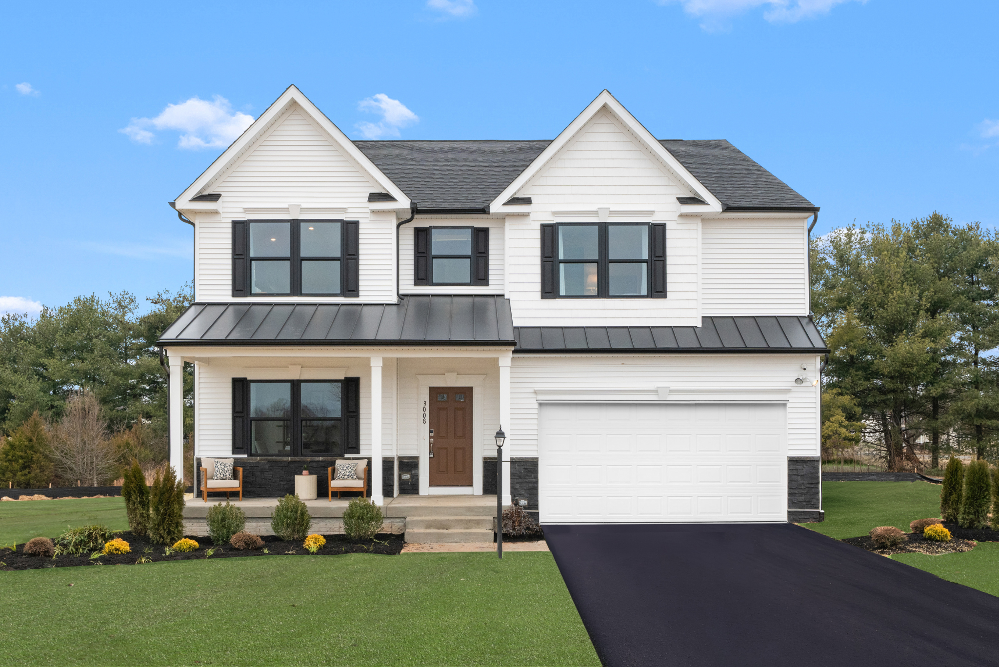 Two-story residential house with a white exterior, black roof, and a garage, surrounded by a well-maintained lawn and landscaped garden.