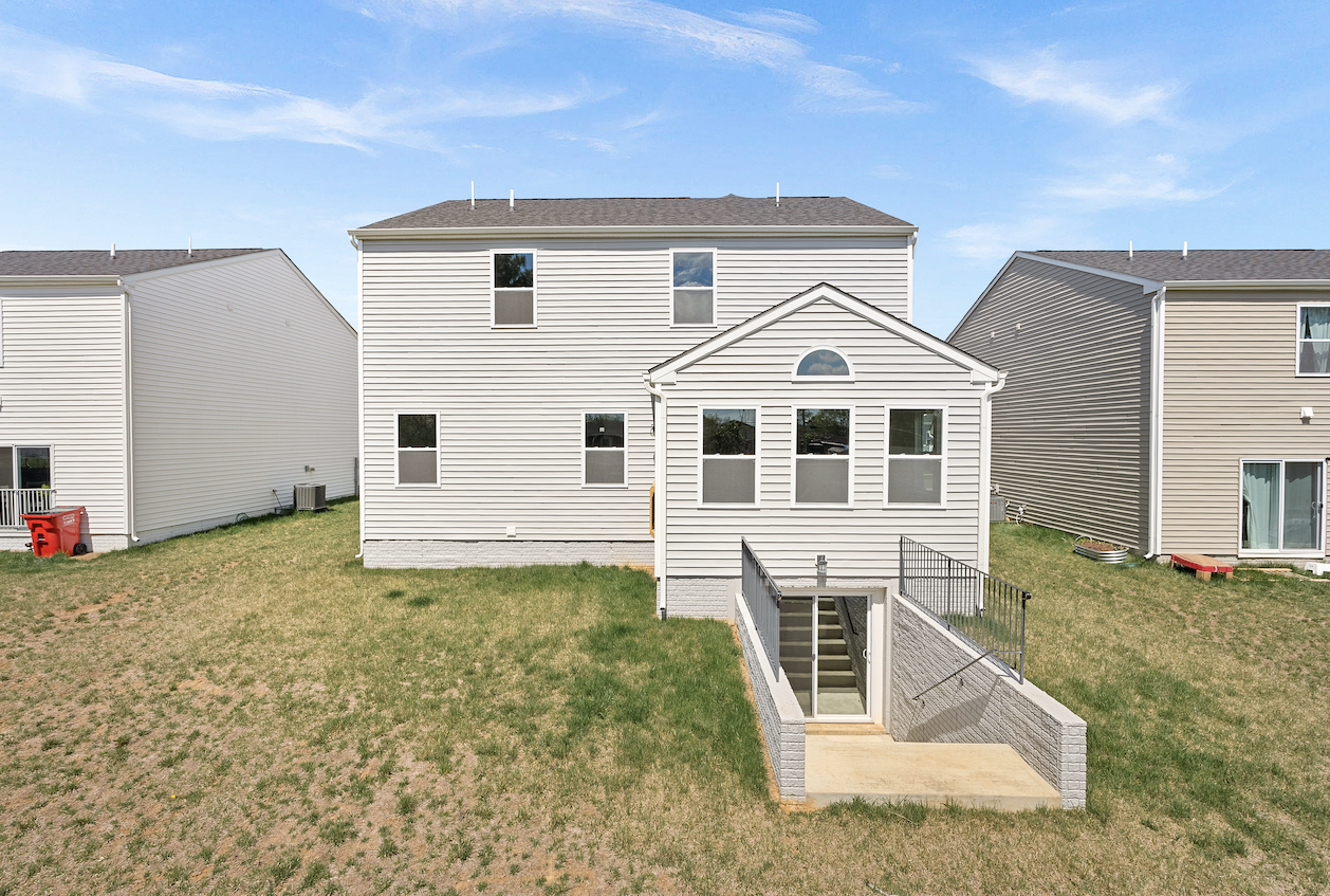 Backyard view of a modern, two-story house with a basement walkout and vinyl siding under a clear blue sky.