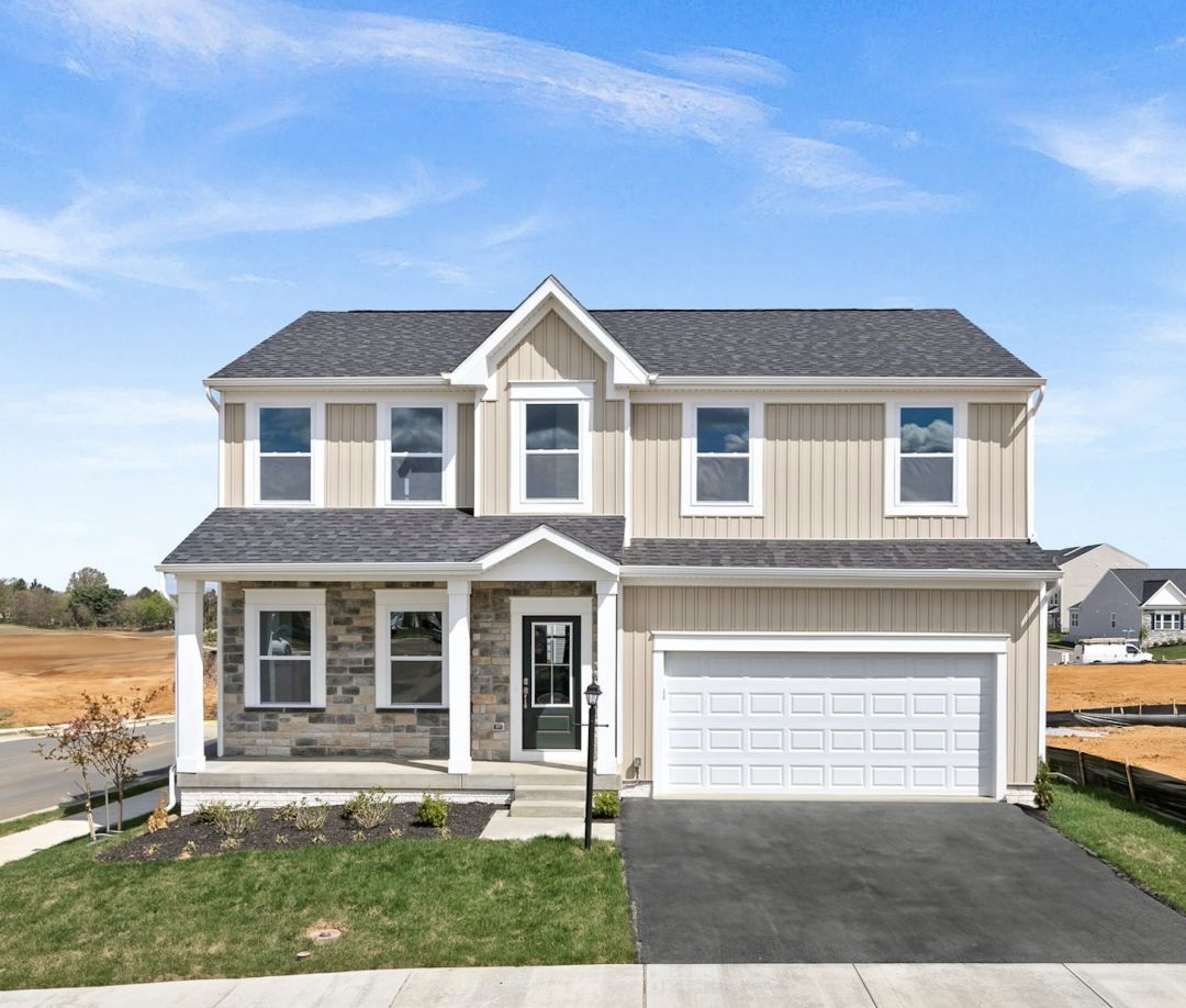 Front view of a modern two-story suburban house with stone and siding exterior, white garage door, and well-maintained lawn under a clear blue sky.
