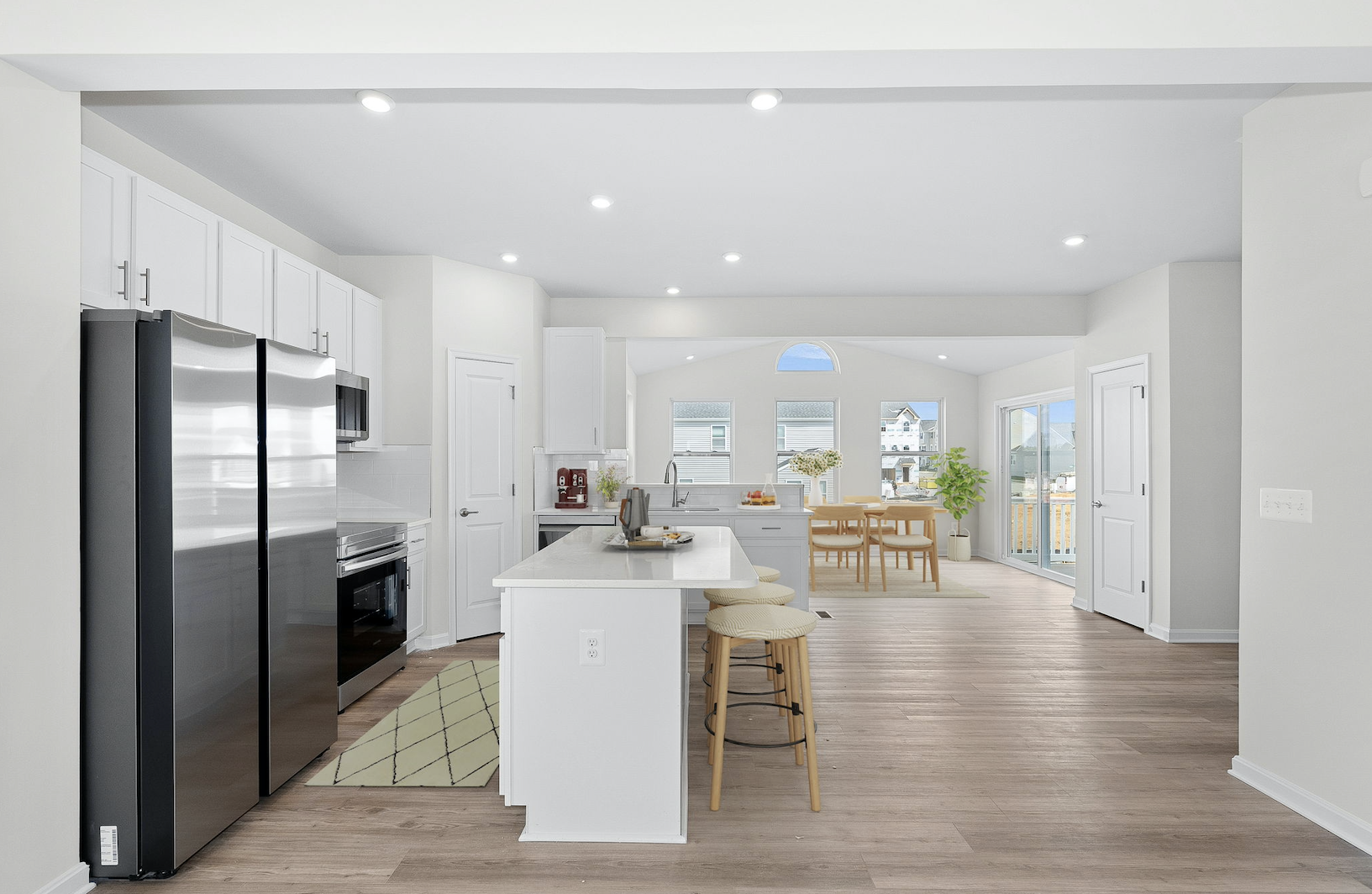 Modern kitchen and dining area with white cabinets, stainless steel appliances, and wooden flooring in a bright, open-concept home.