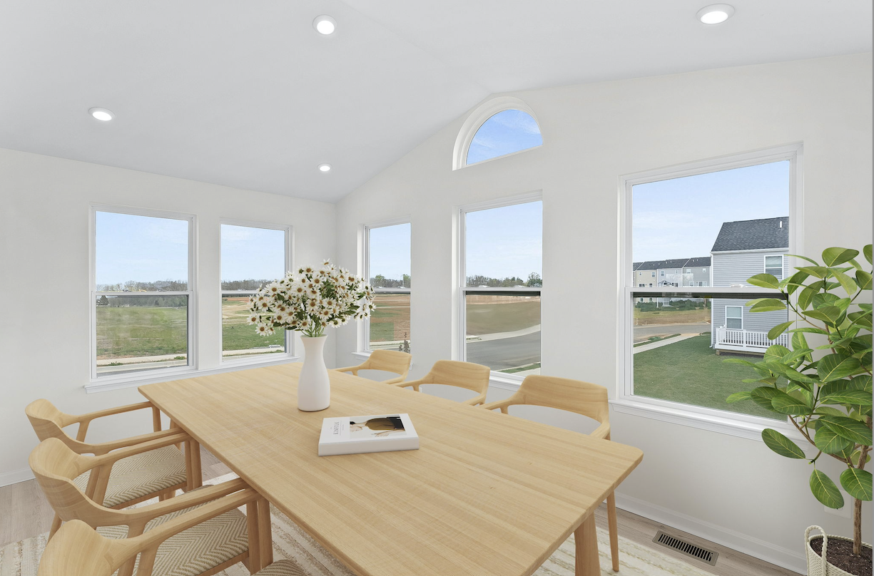 Bright dining room with a modern wooden table, elegant chairs, a vase of daisies, and large windows overlooking a suburban landscape.