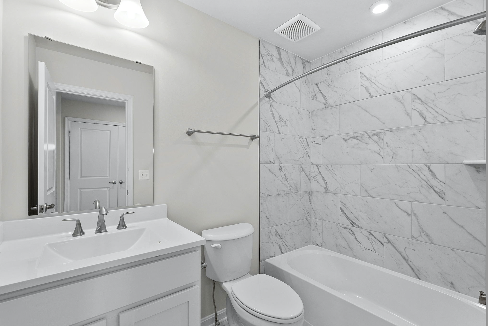 Modern bathroom with white vanity, marble tile bathtub, and sleek fixtures.