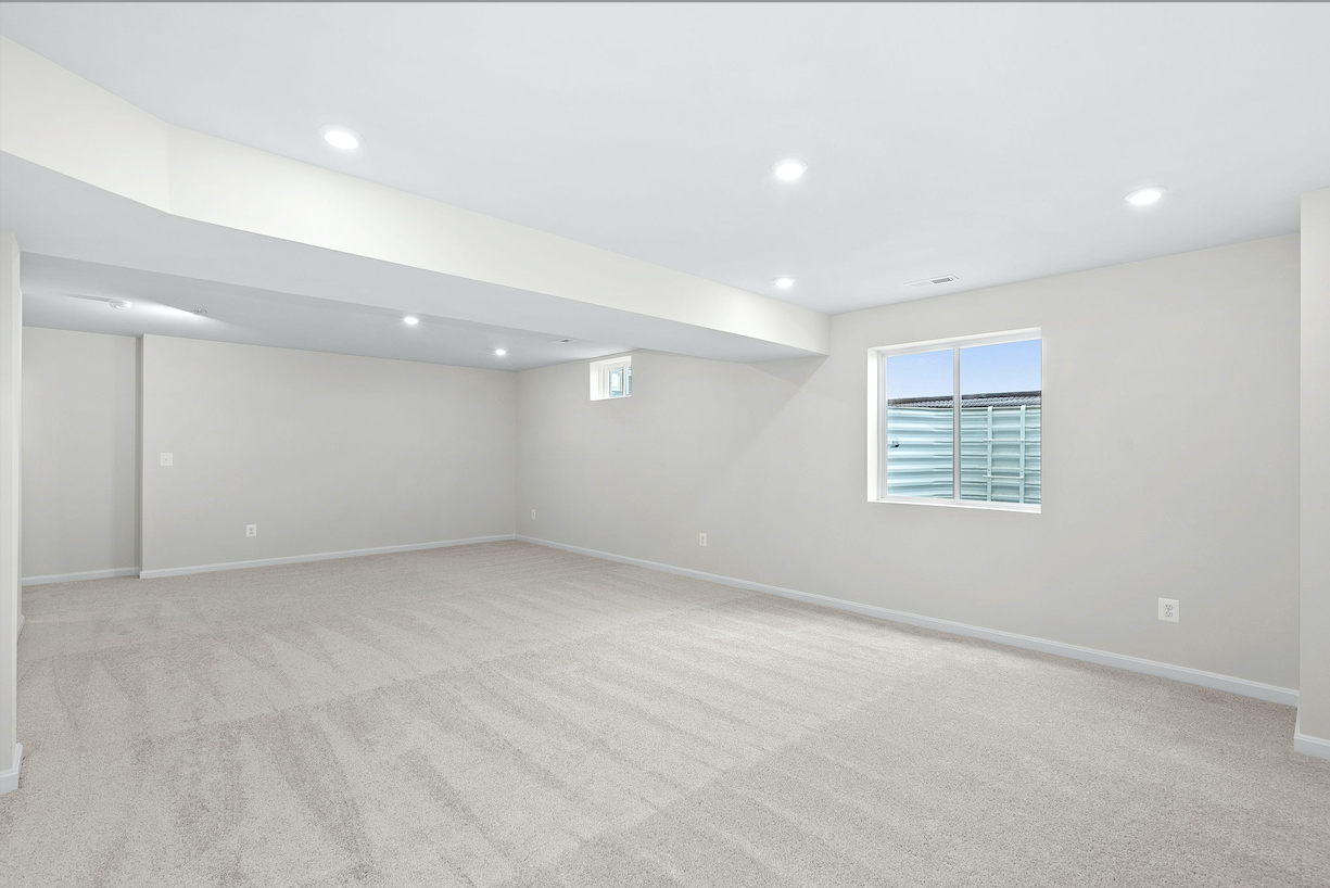 Spacious, carpeted basement room with recessed lighting and two windows, showcasing a modern and minimalistic design.