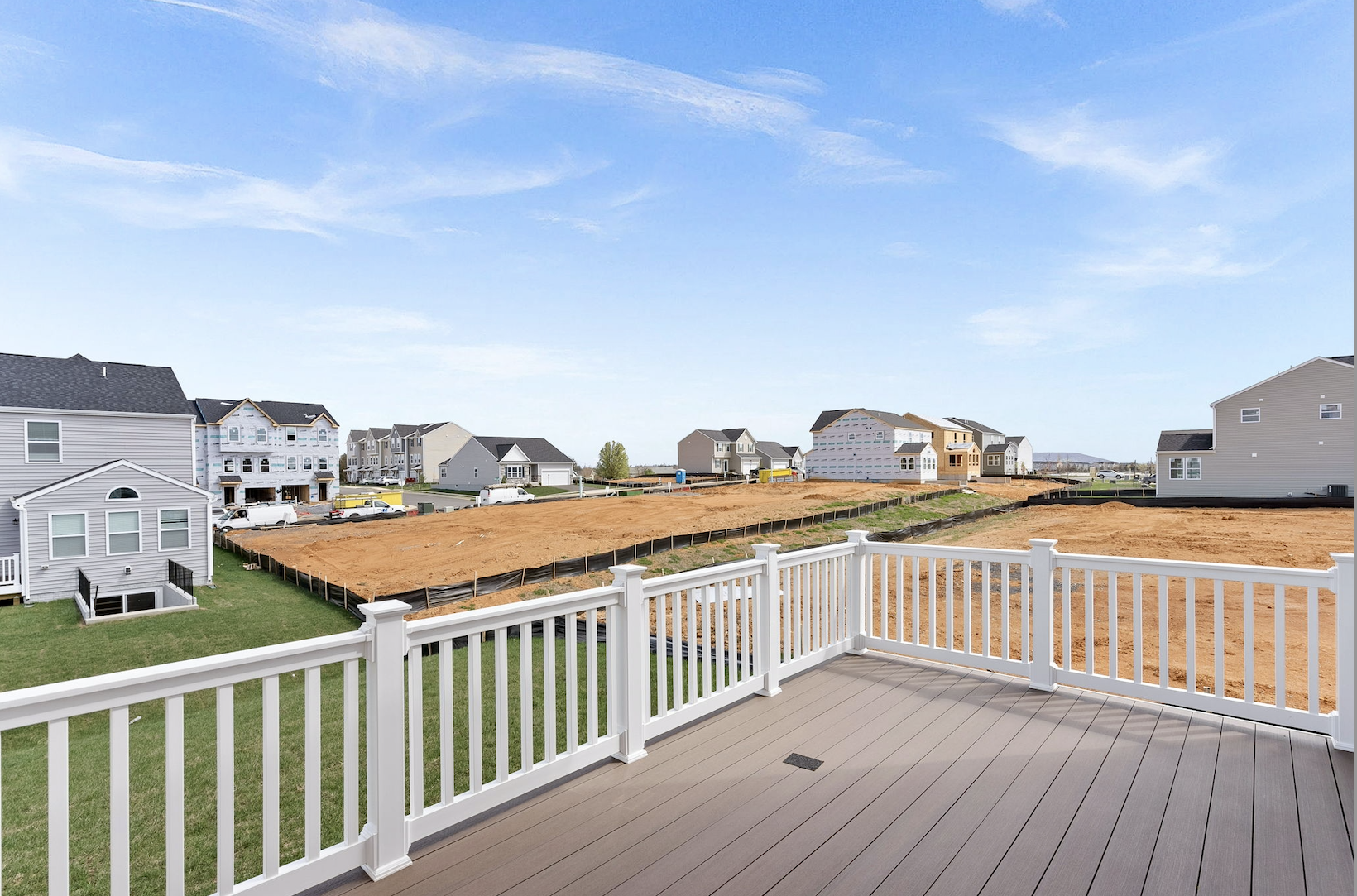 New residential neighborhood under construction viewed from a deck with white railings on a sunny day.