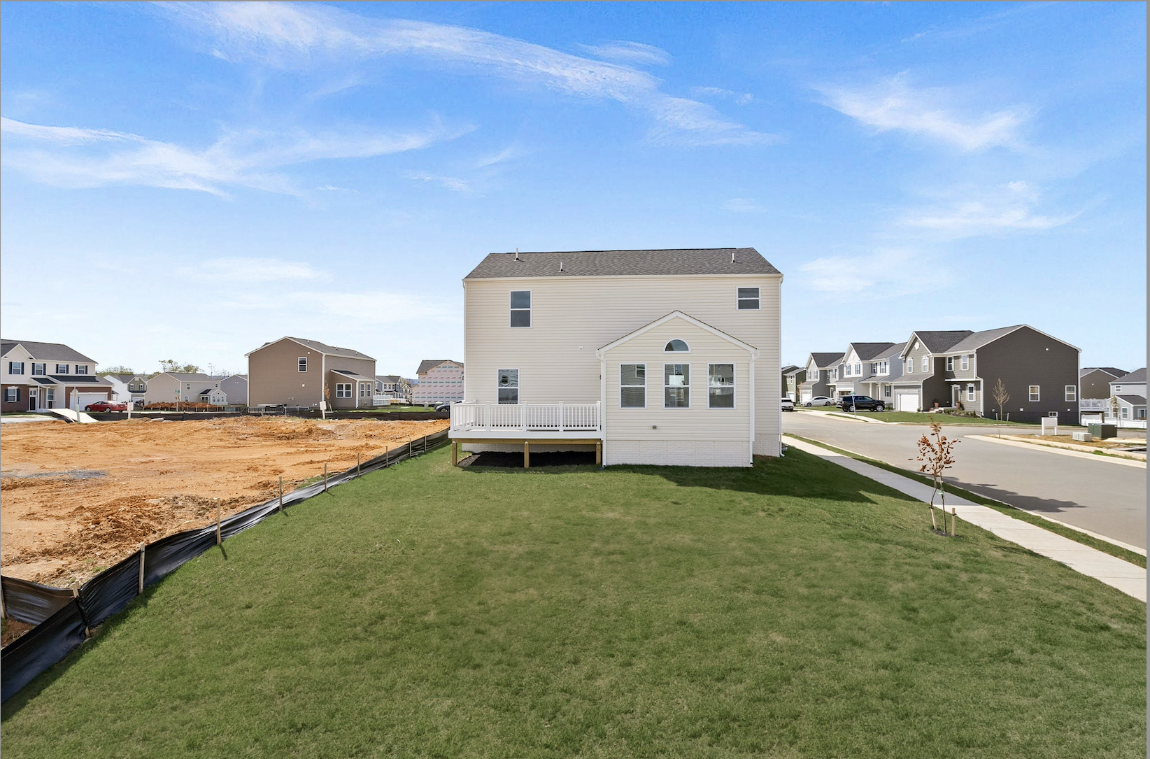 Newly constructed suburban home with a spacious backyard, surrounded by ongoing residential development under a clear blue sky.