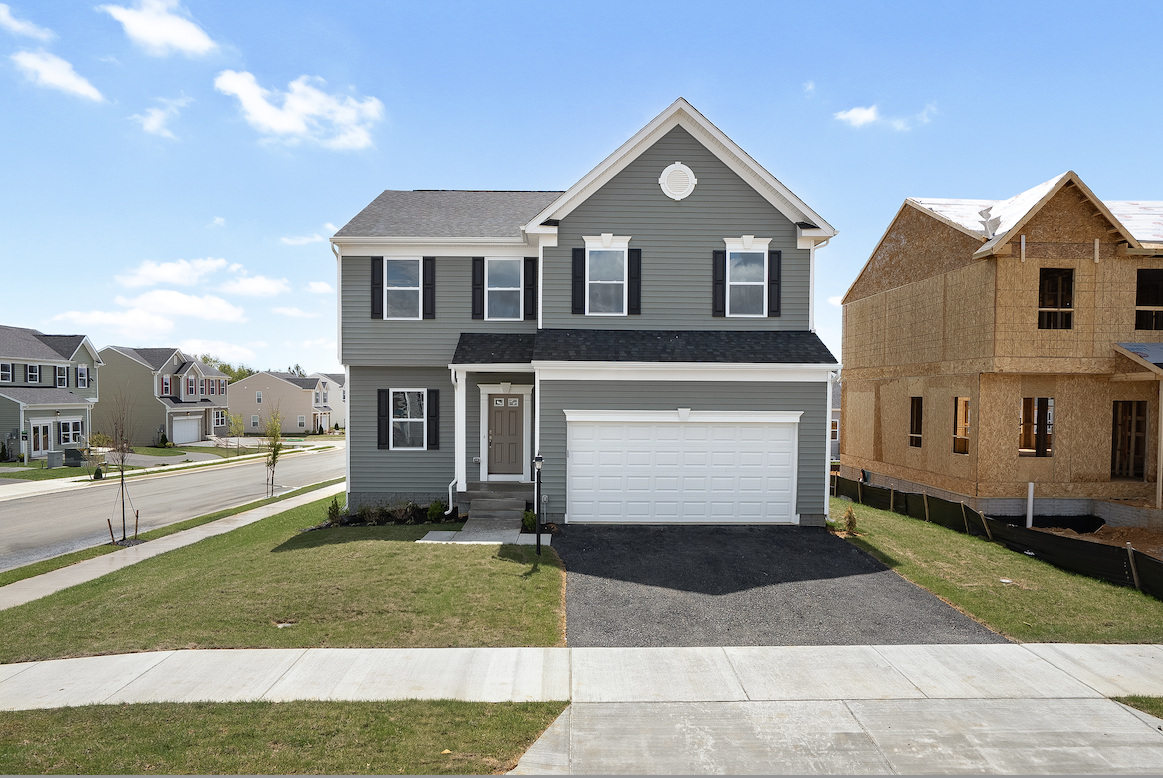Newly constructed two-story gray suburban house with a garage, situated on a corner lot next to another home under construction.