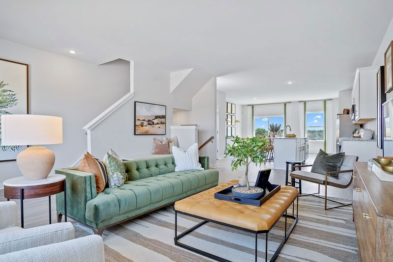 Modern open-concept living room with green velvet sofa, stylish decor, and natural light from large windows.