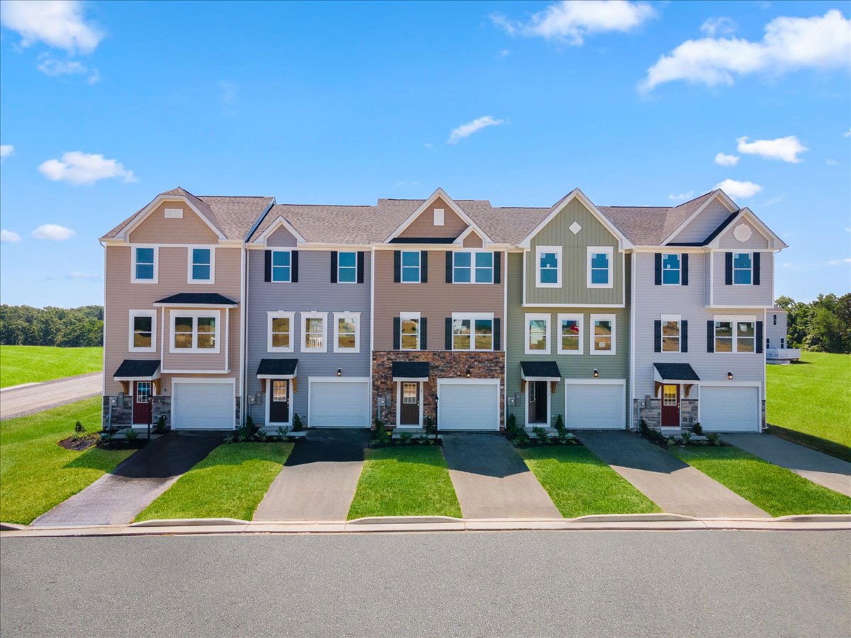 Row of colorful townhouse apartments with garages and landscaped lawns under a clear blue sky.