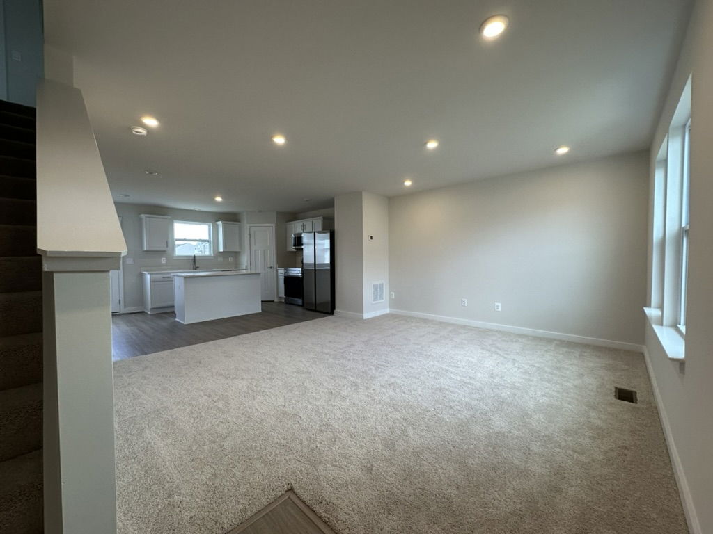Spacious living room featuring modern kitchen appliances, soft carpet, and large windows for natural light.