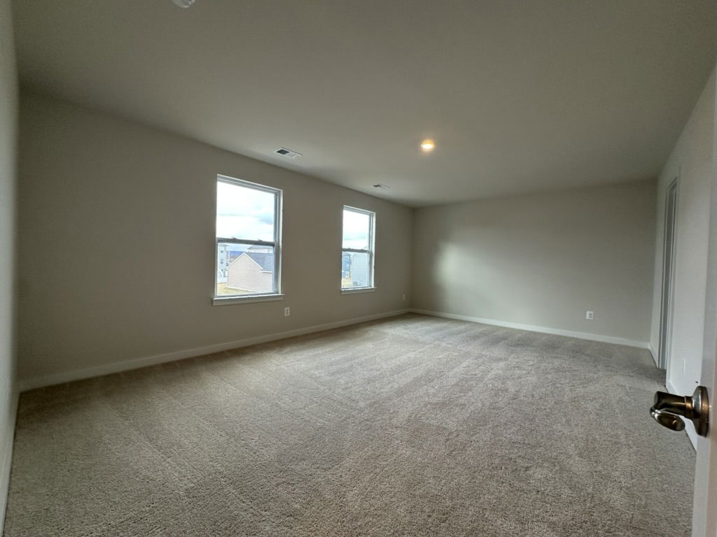 Spacious carpeted living room with natural light from large windows and neutral walls.