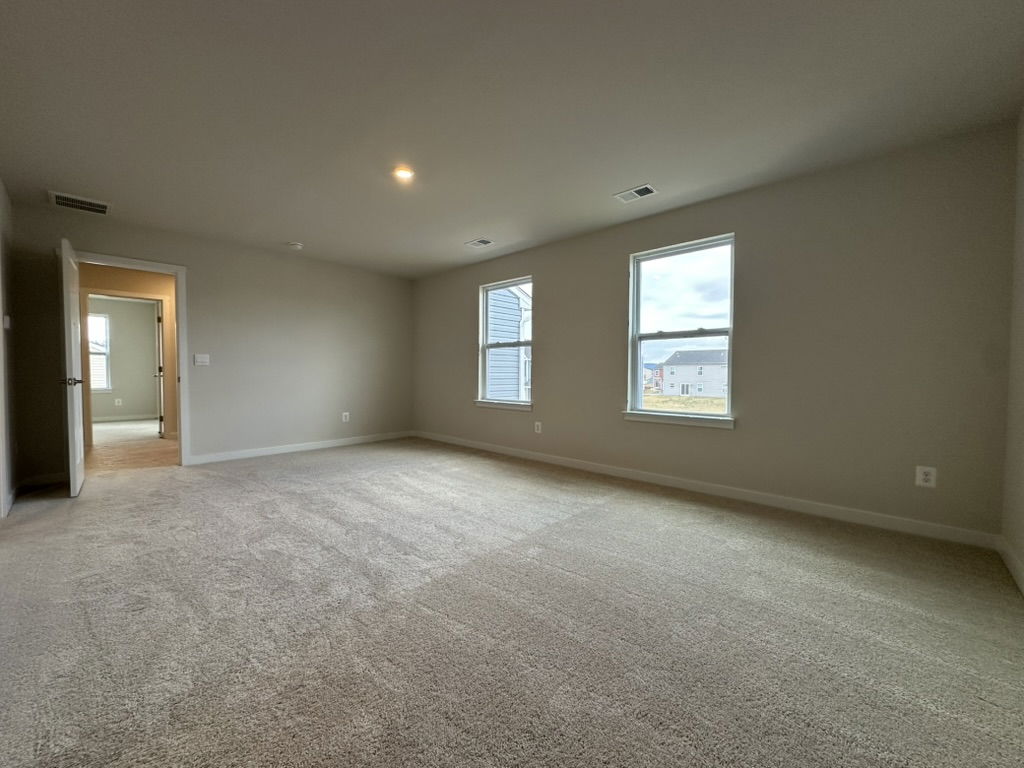Spacious light-filled living room with beige carpet and two windows, showcasing a modern home interior.